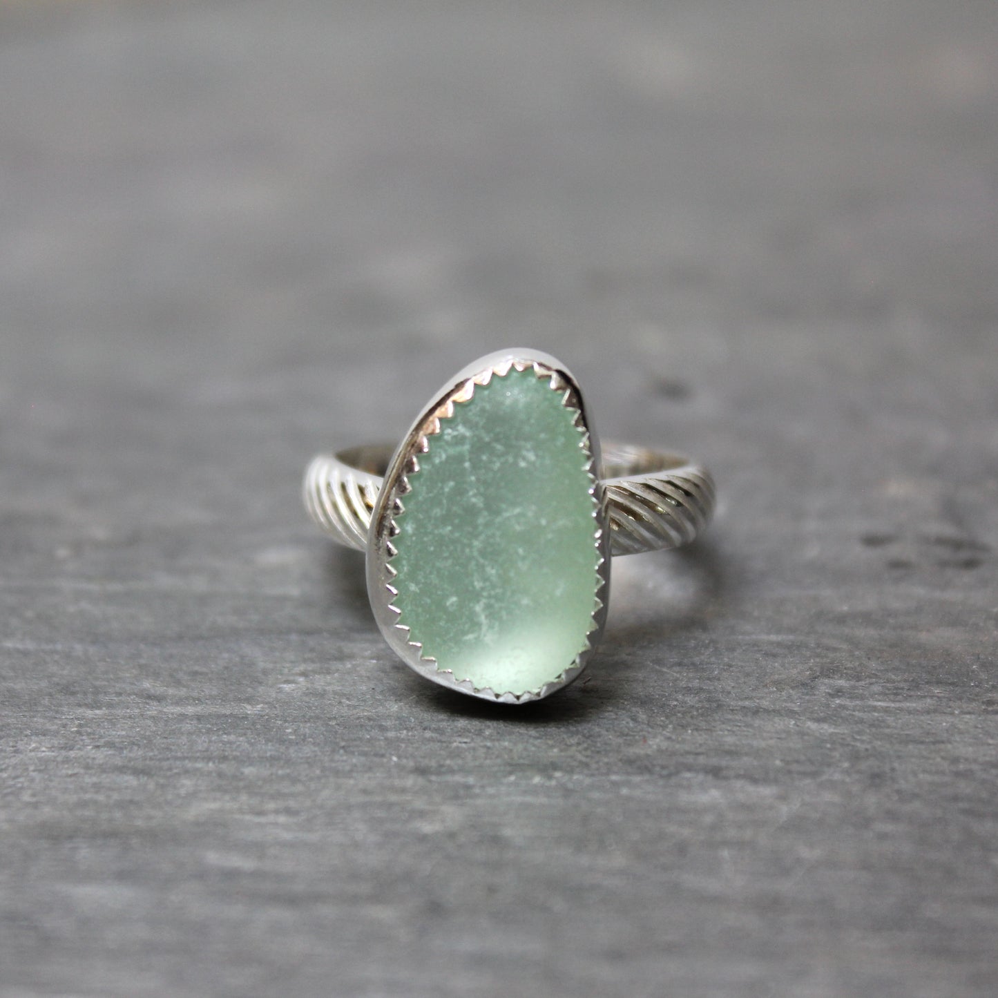 Silver ring with a greenish sea glass on a gray surface