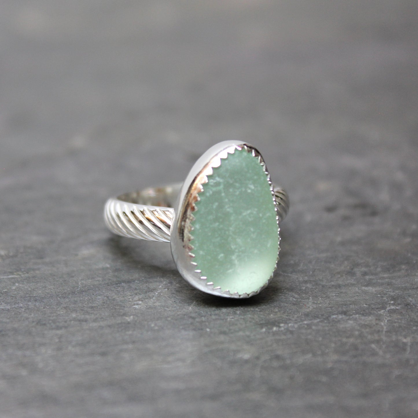 Green  sea glass ring with silver band on a gray background
