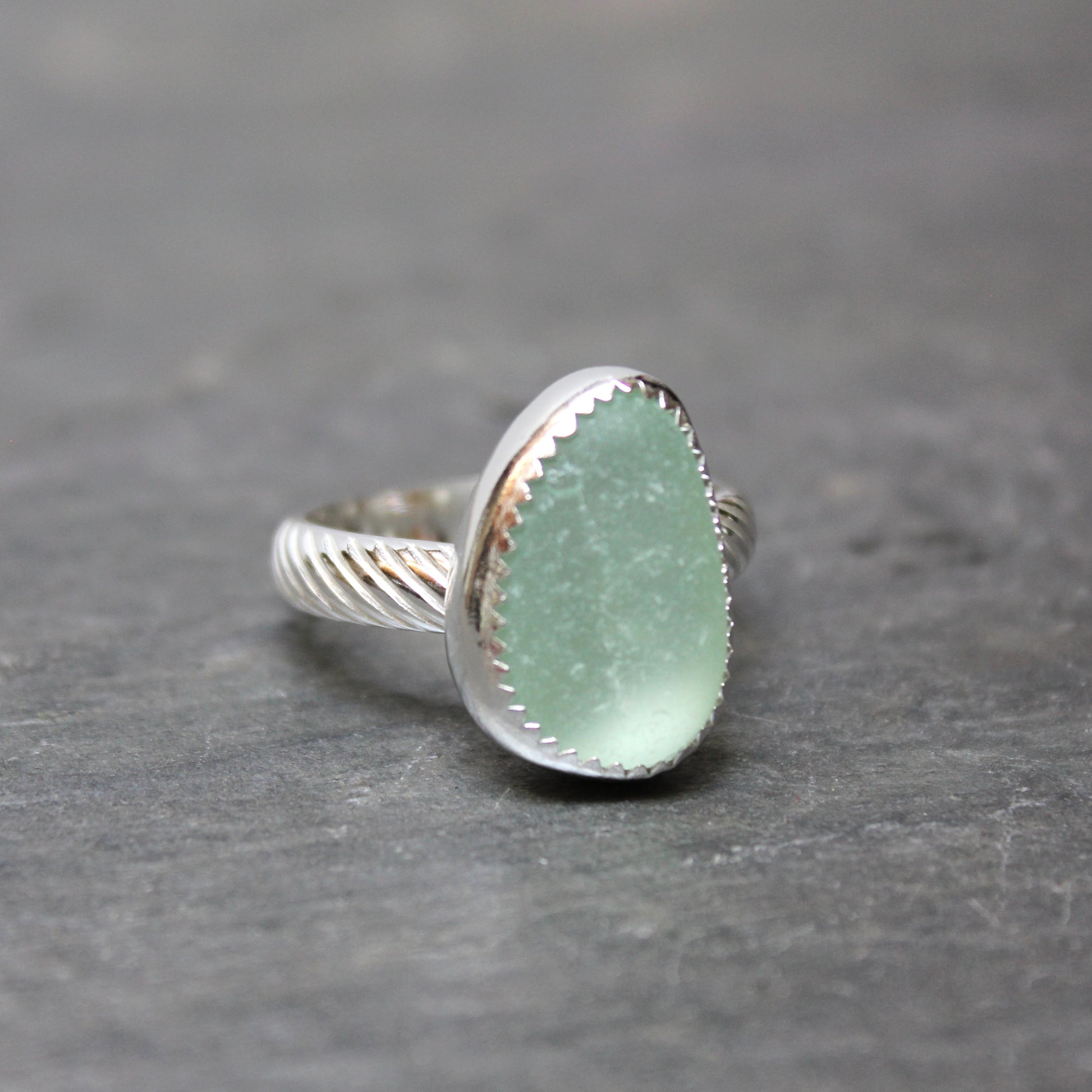 Green  sea glass ring with silver band on a gray background