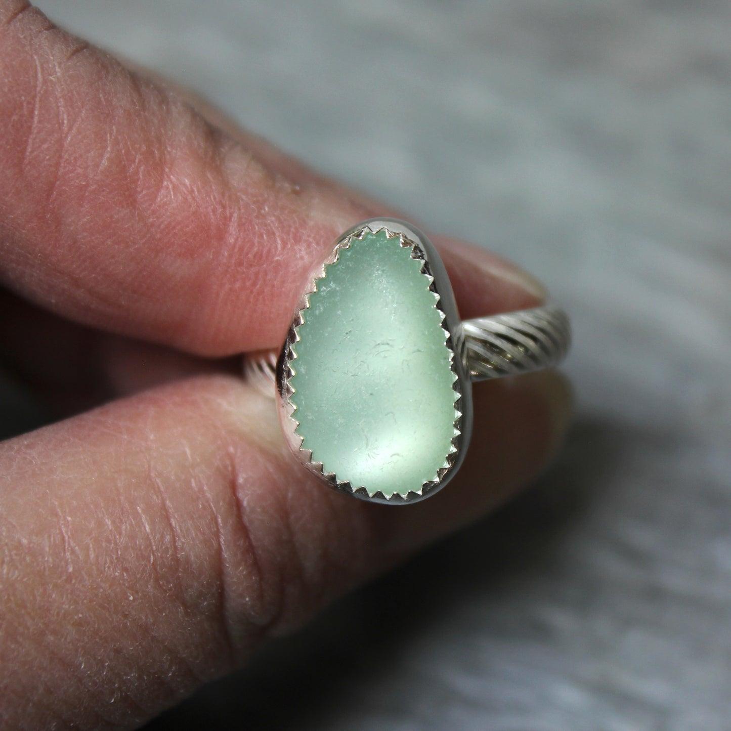 Green sea glass ring with silver band on a finger against a neutral background