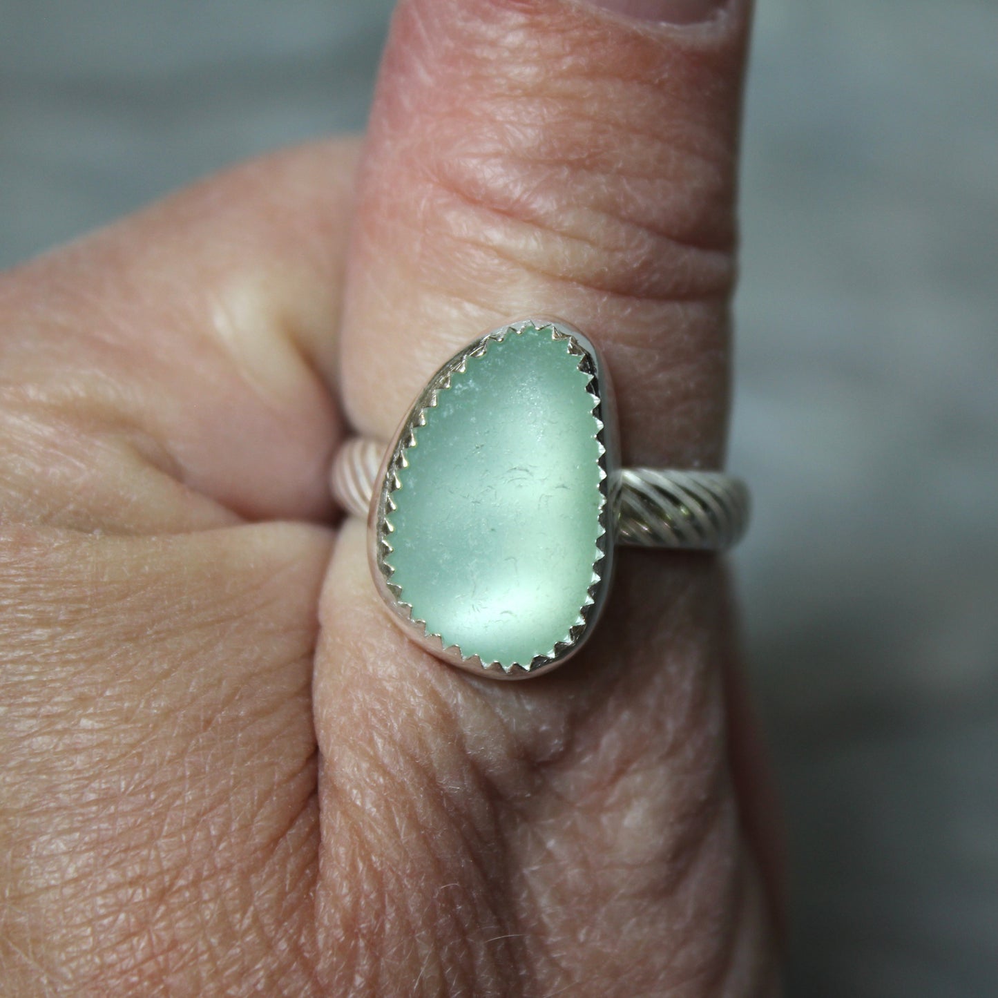 Close-up of a hand wearing a silver band with a green sea glass.