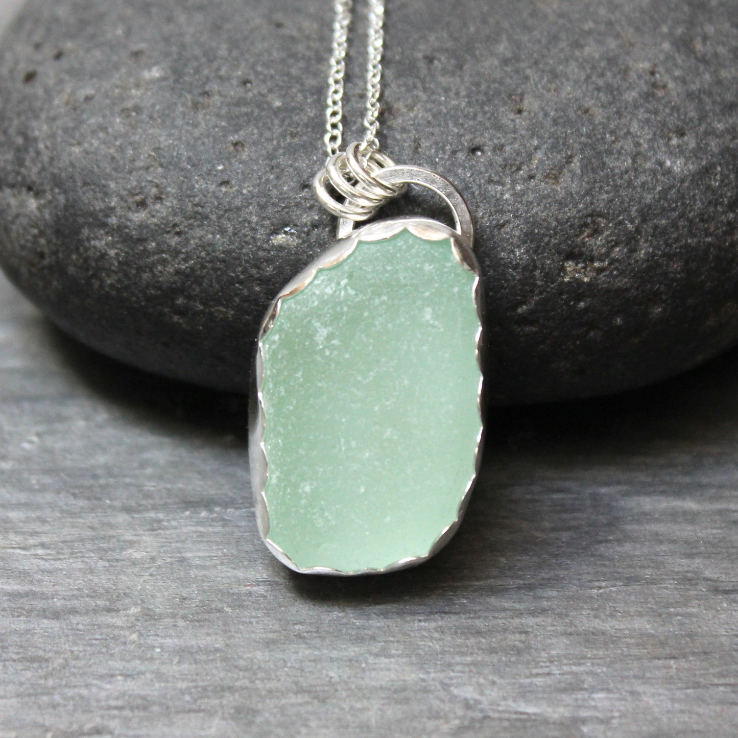 Green sea glass pendant necklace on a stone background