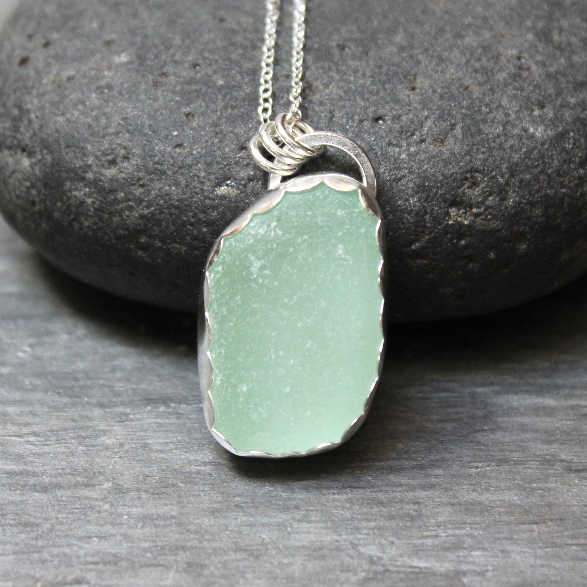 Green sea glass pendant necklace on a stone background