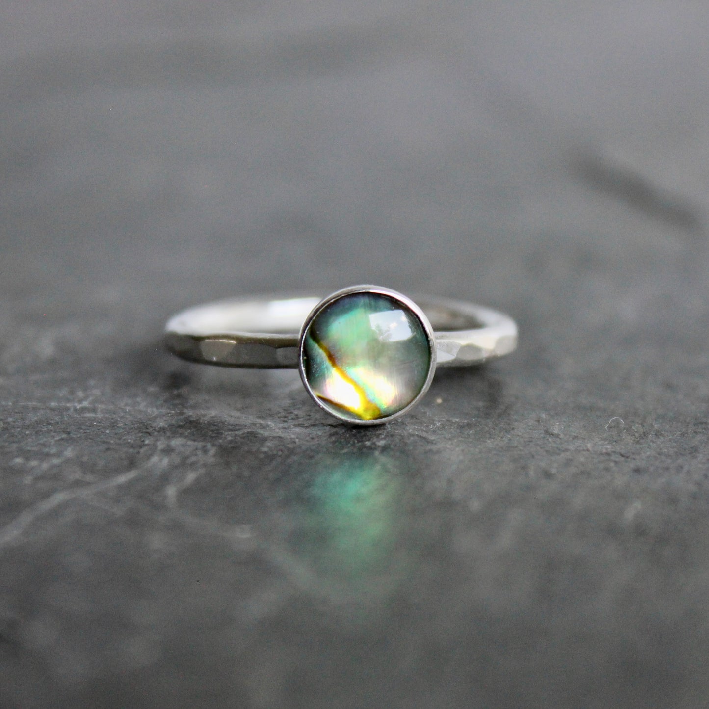 Silver ring with a green abalone cabochon on a gray surface