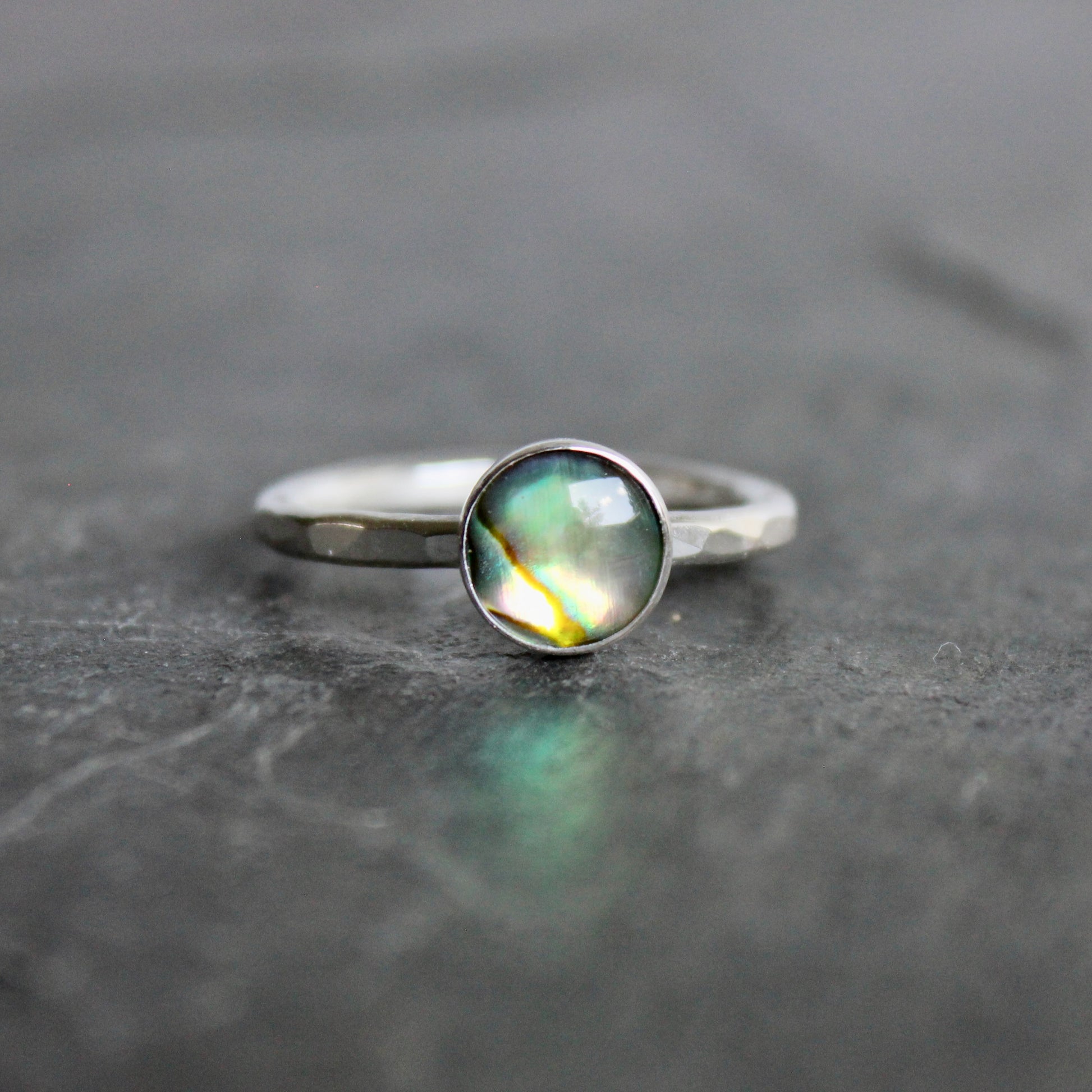 Silver ring with a green abalone cabochon on a gray surface