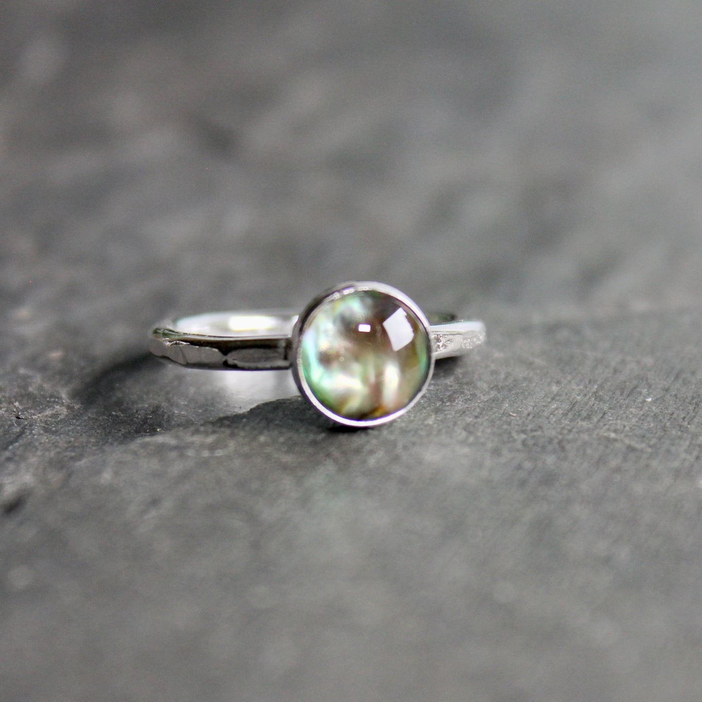 Silver ring with a green abalone cabochon on a gray surface