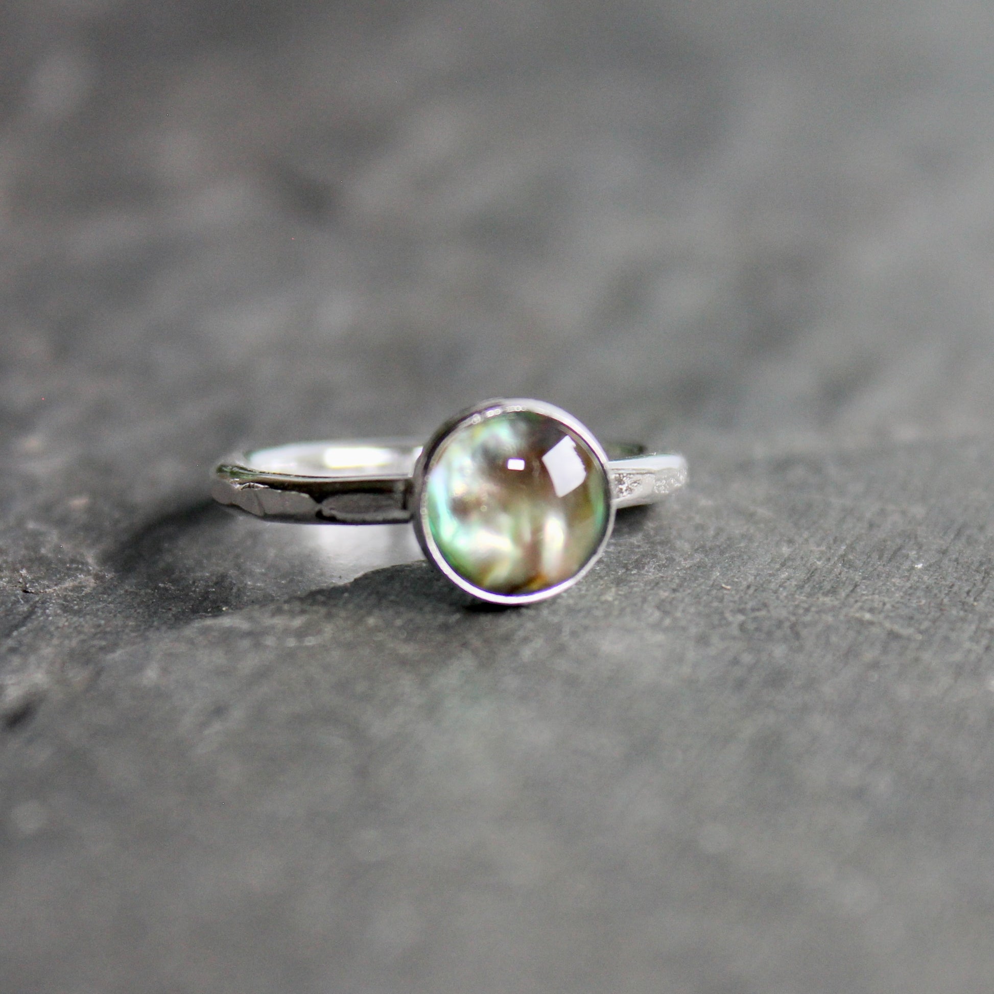 Silver ring with a green abalone cabochon on a gray surface