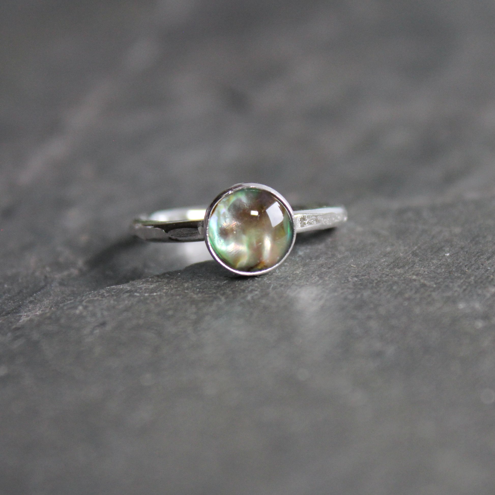 Silver ring with a green abalone cabochon on a gray surface