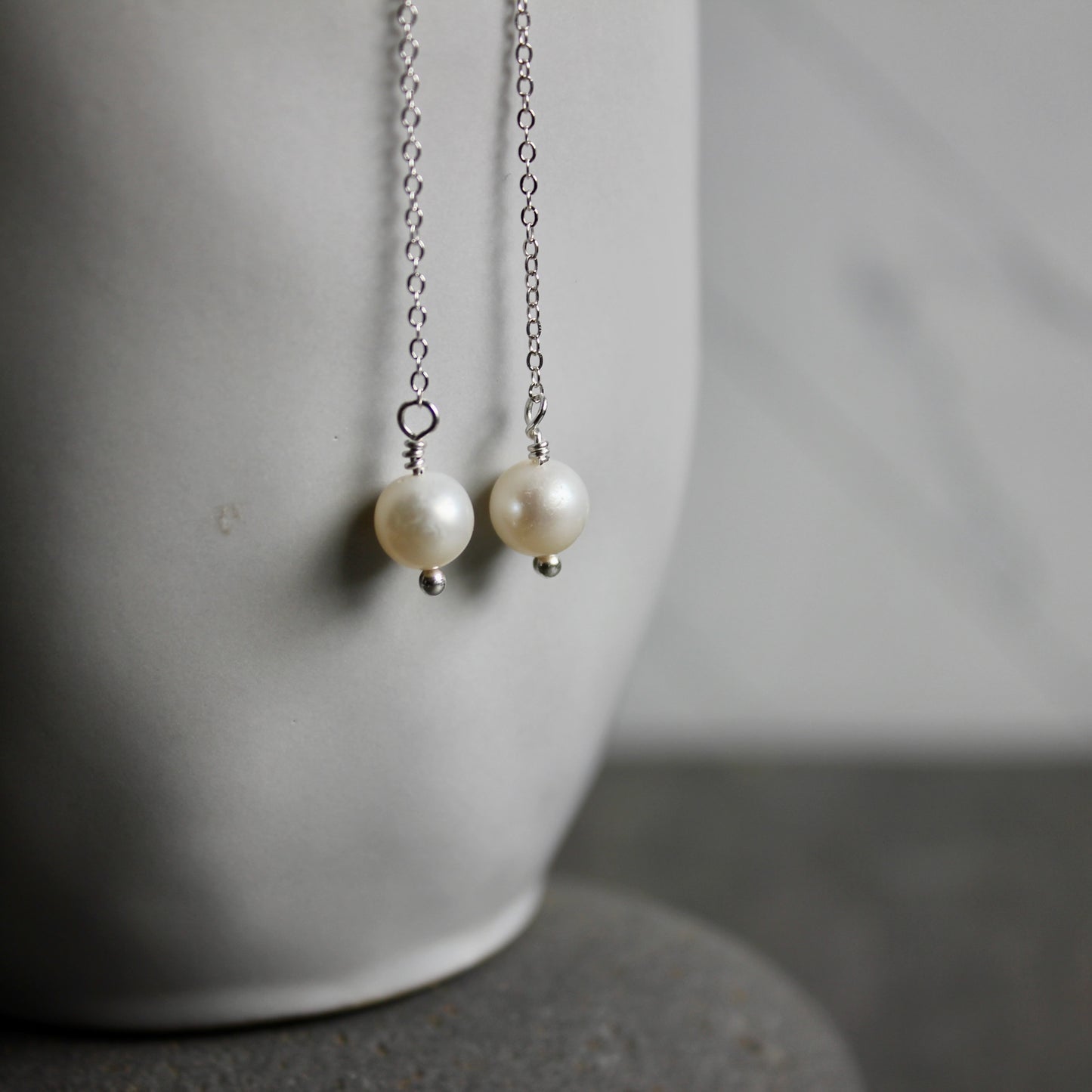 Pearl earrings with silver chain on a neutral background
