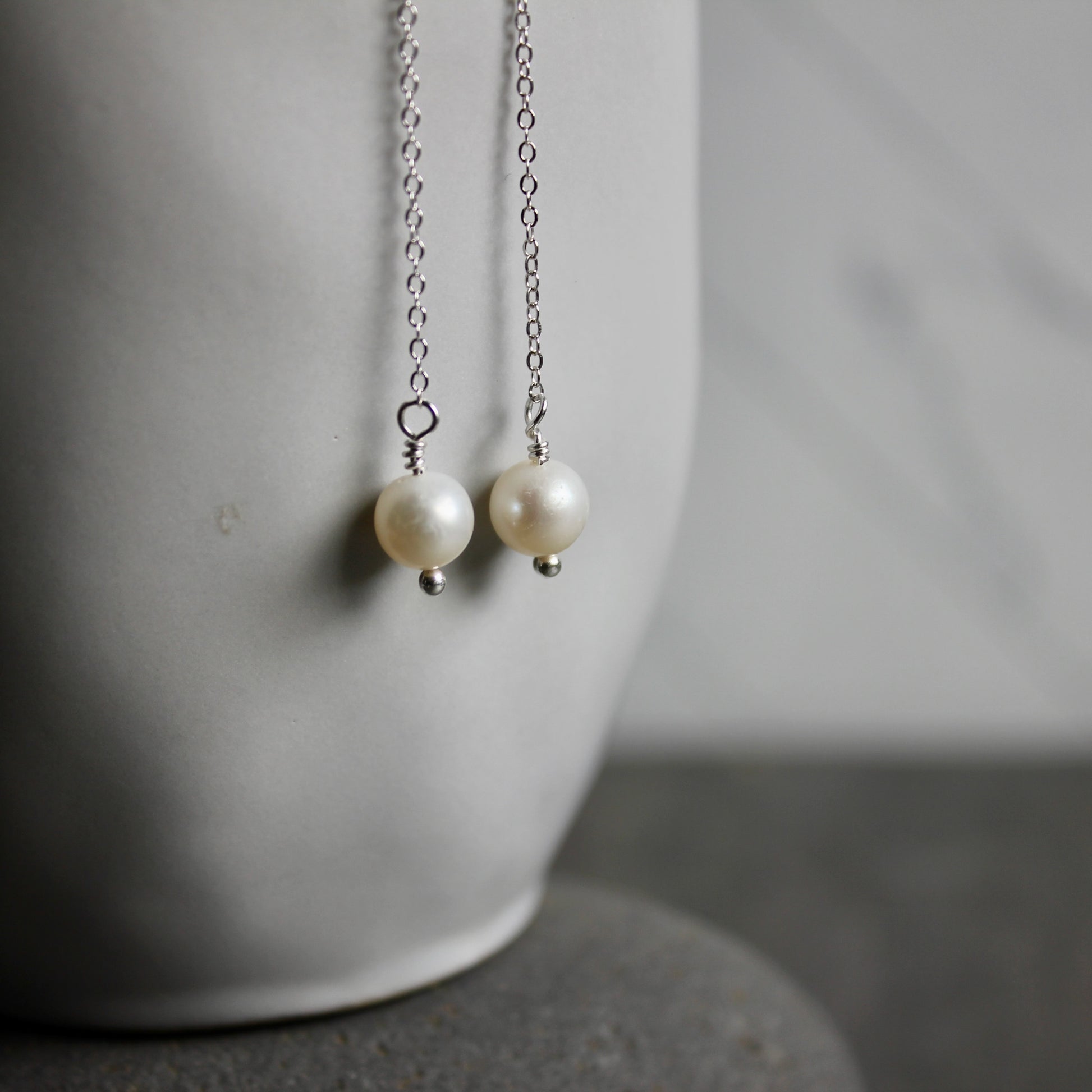 Pearl earrings with silver chain on a neutral background