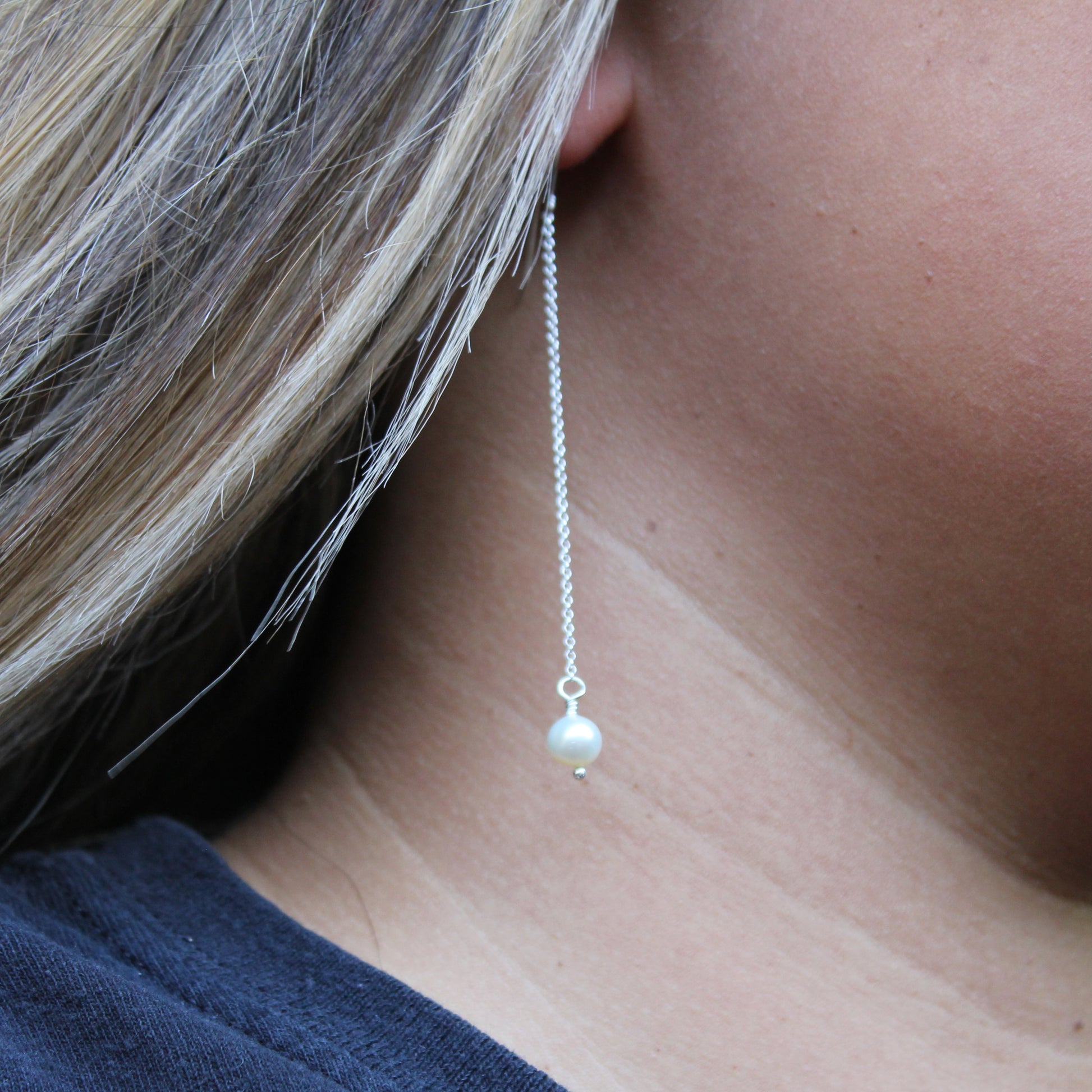 Pearl drop earring worn by a person with blonde hair.