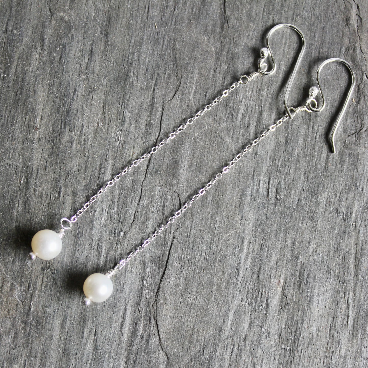 Silver earrings with pearl beads on a gray stone surface