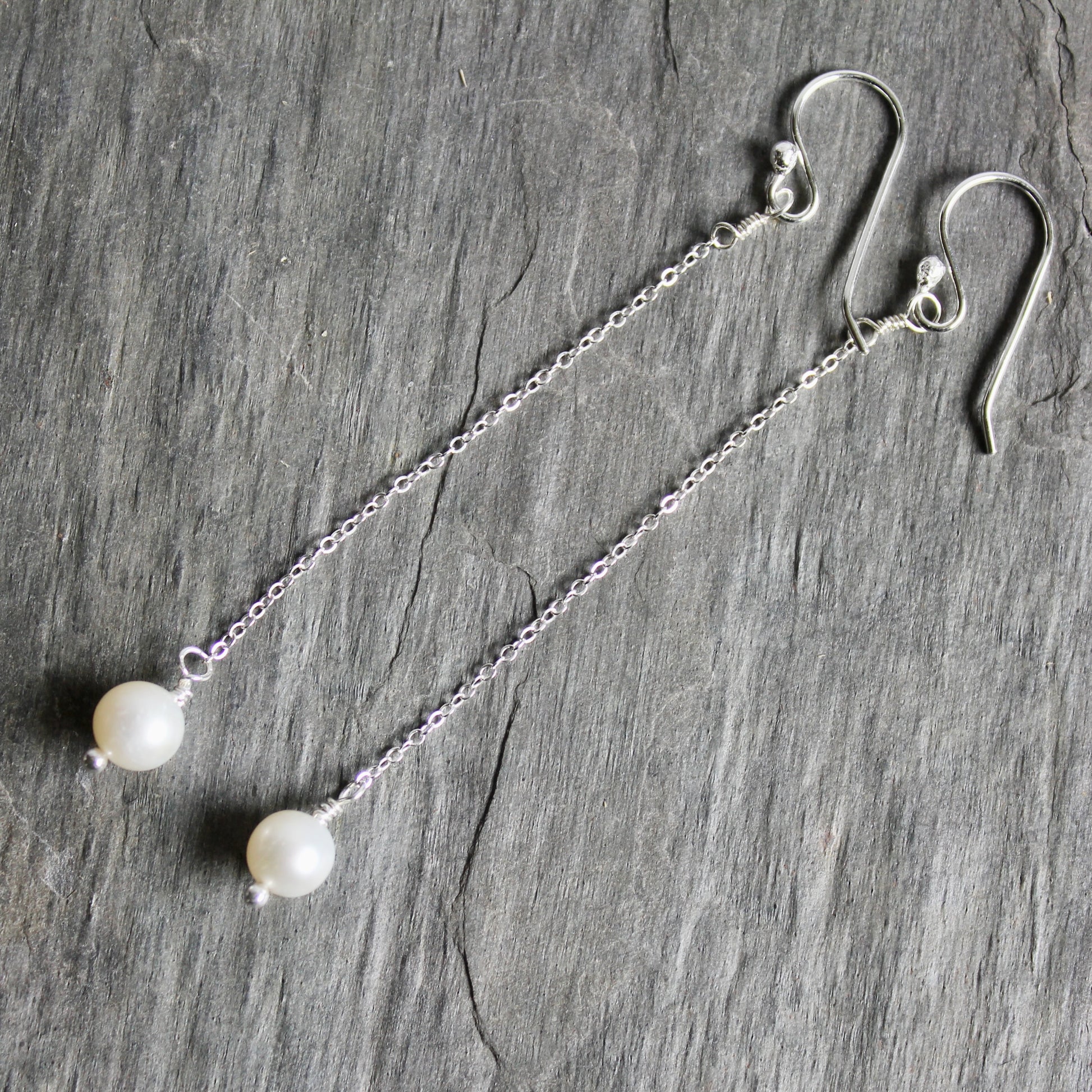 Silver earrings with pearl beads on a gray stone surface