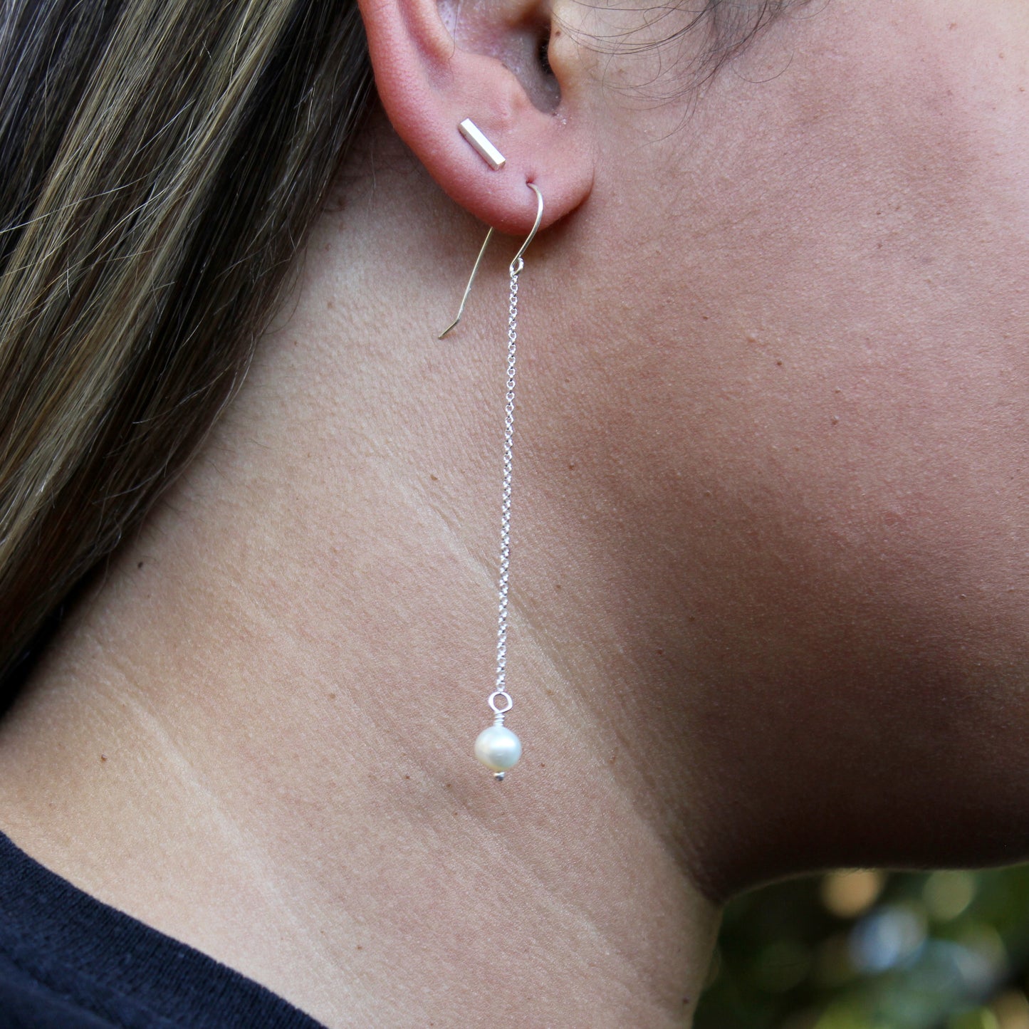Close-up of a pearl drop earring on an ear with a blurred background