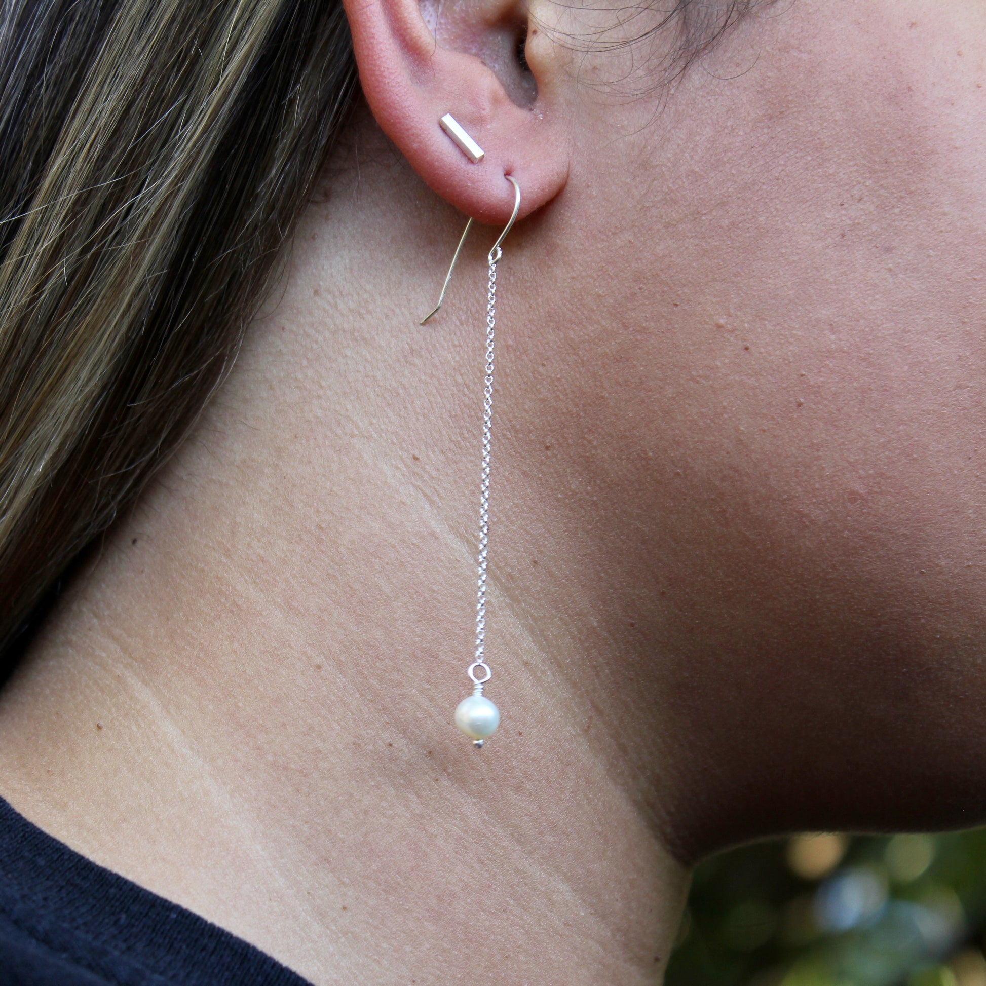 Close-up of a pearl drop earring on an ear with a blurred background
