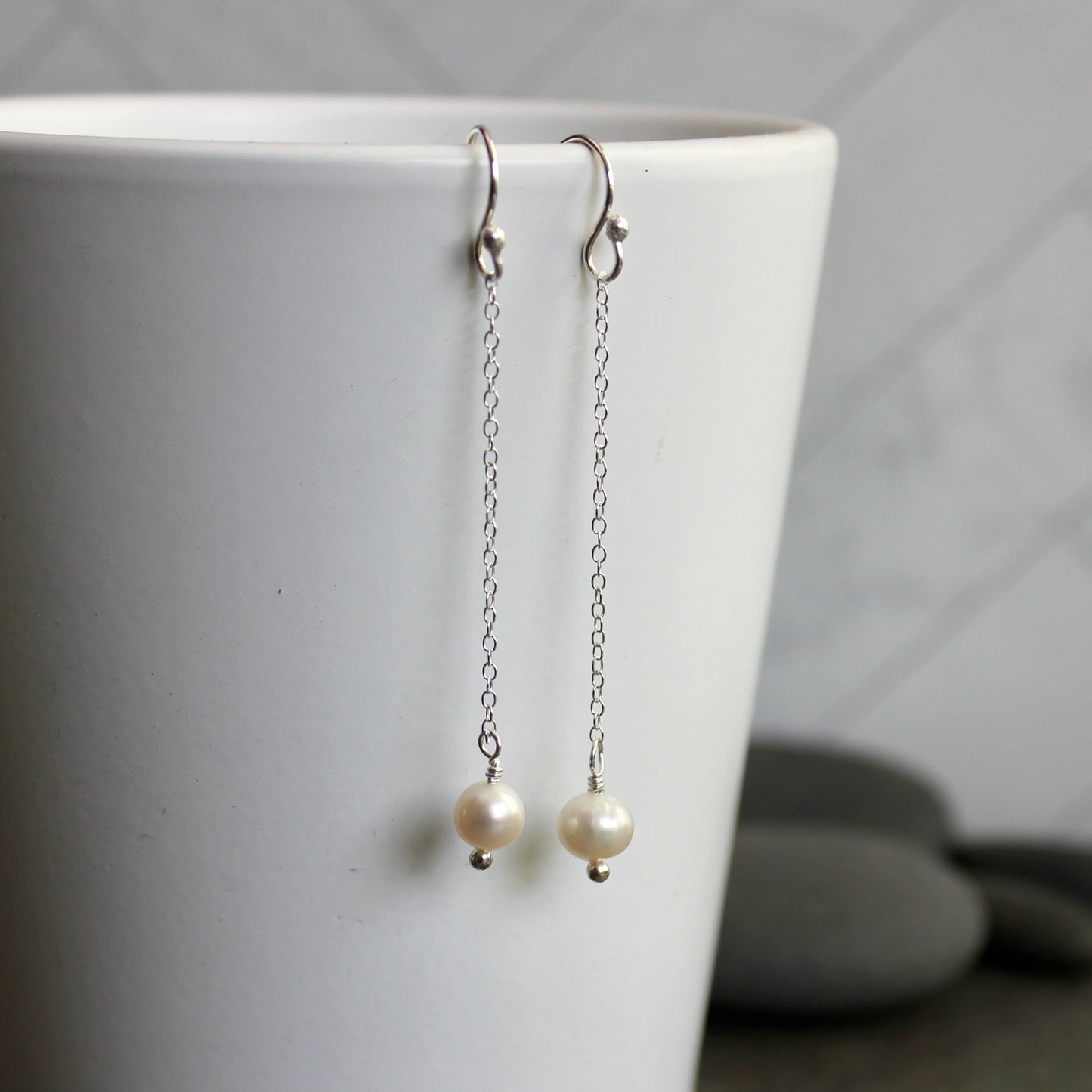 Pearl earrings hanging from a white cup against a neutral background