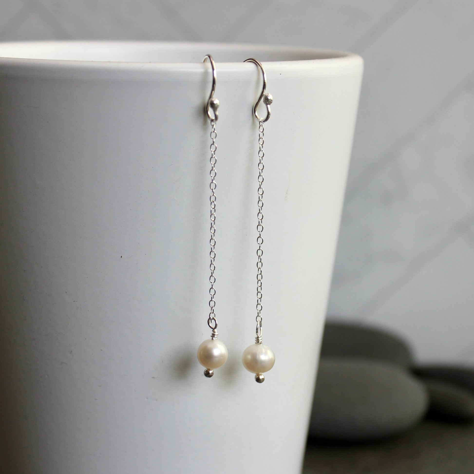 Pearl earrings hanging from a white cup against a neutral background