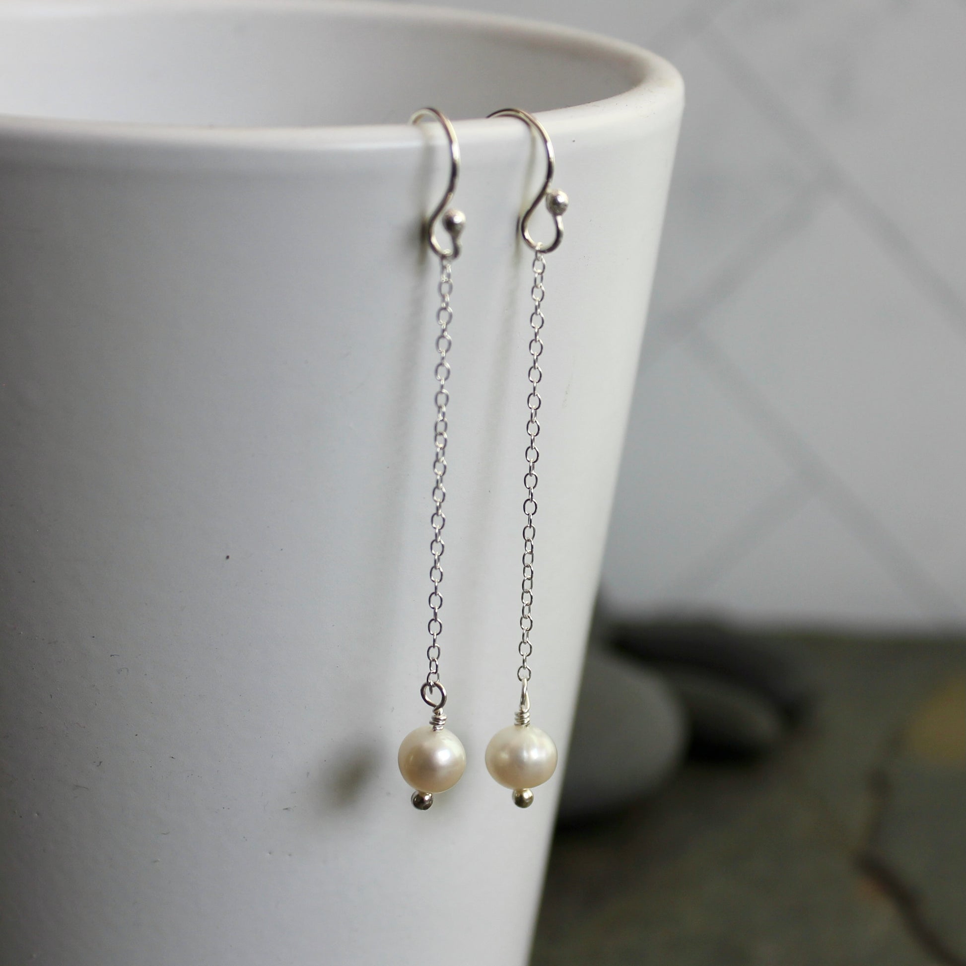 Pearl earrings hanging from a white cup on a neutral background