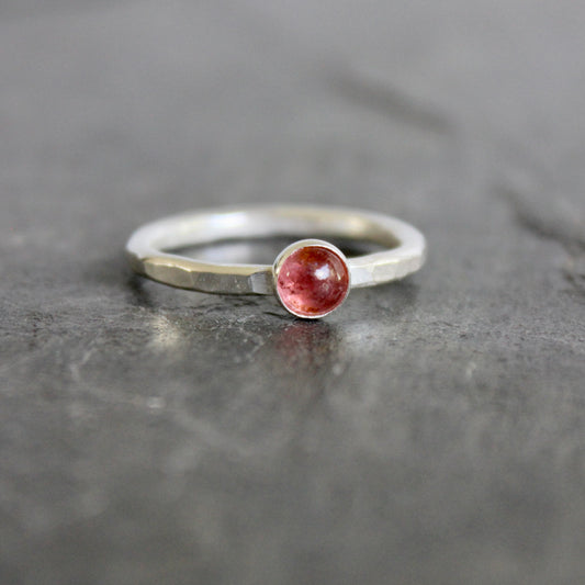 Silver ring with a small round pink tourmaline on a gray surface
