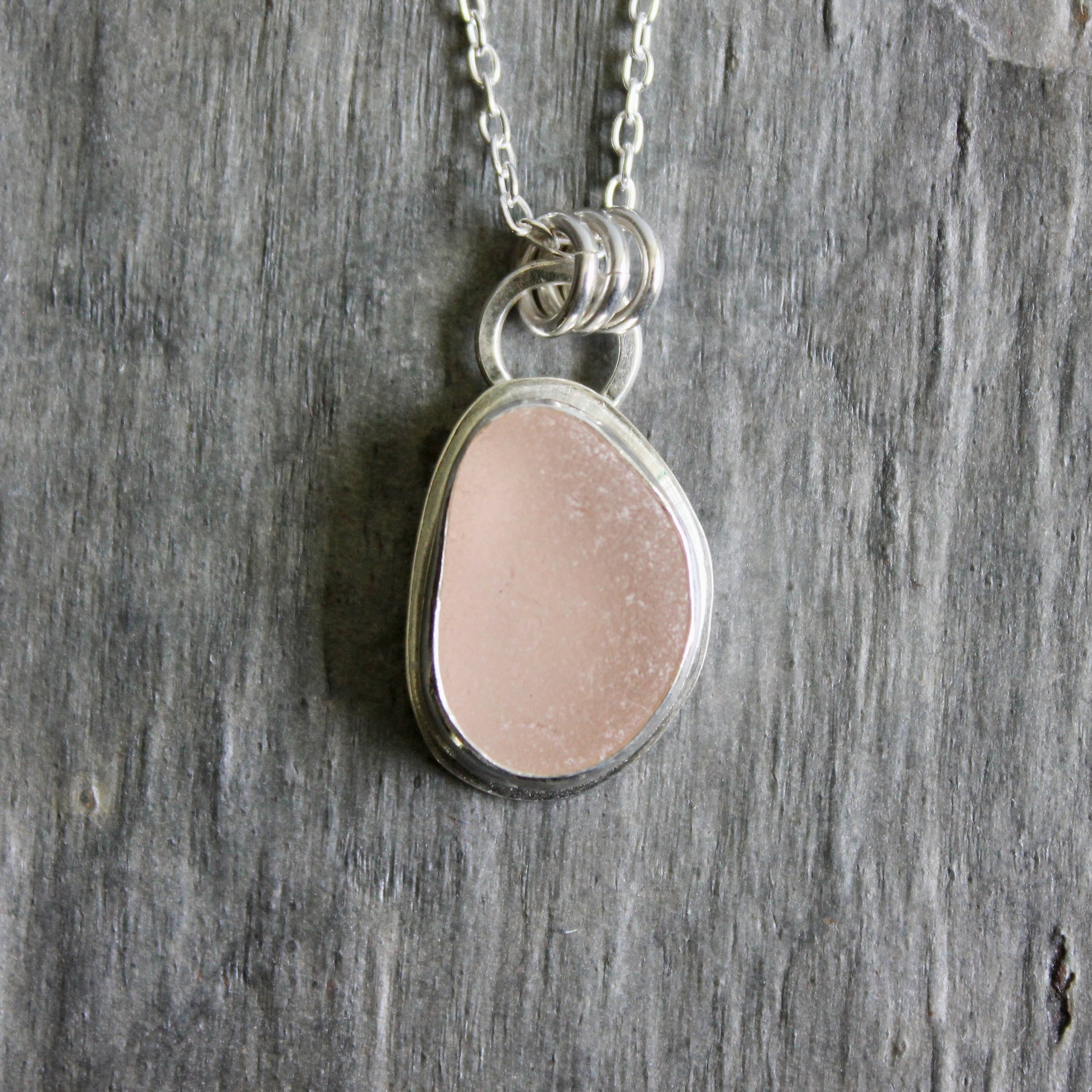 Necklace with a pink sea glass on a wooden surface