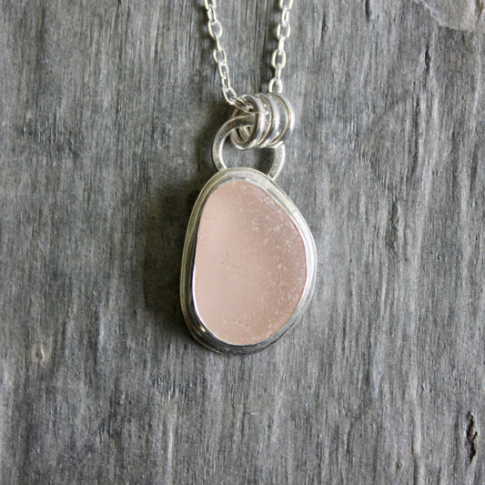 Necklace with a pink sea glass on a wooden surface