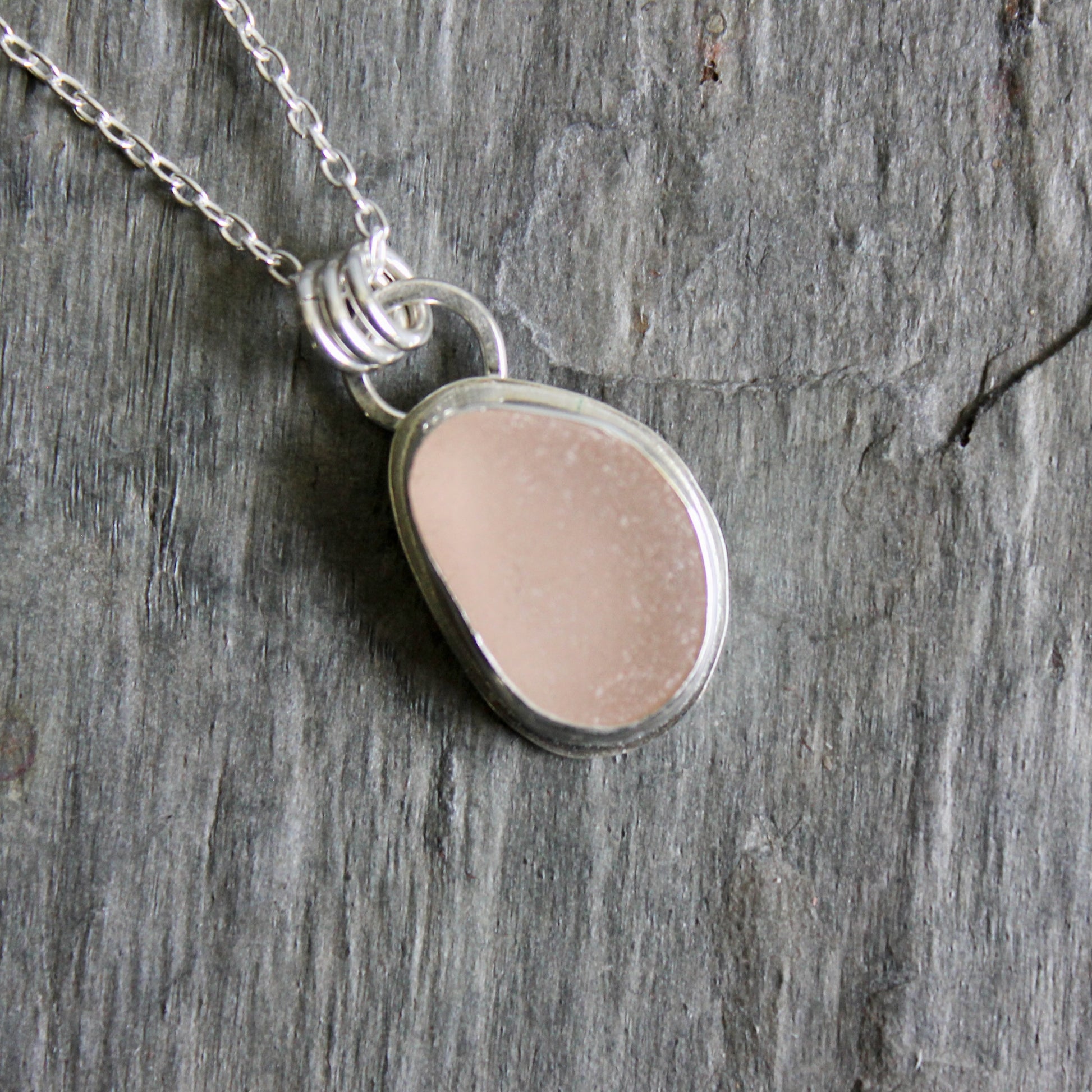 Necklace with a pink sea glass on a wooden surface