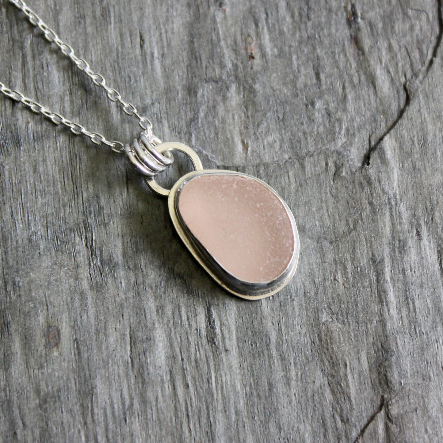 Necklace with a pink sea glass on a gray stone surface