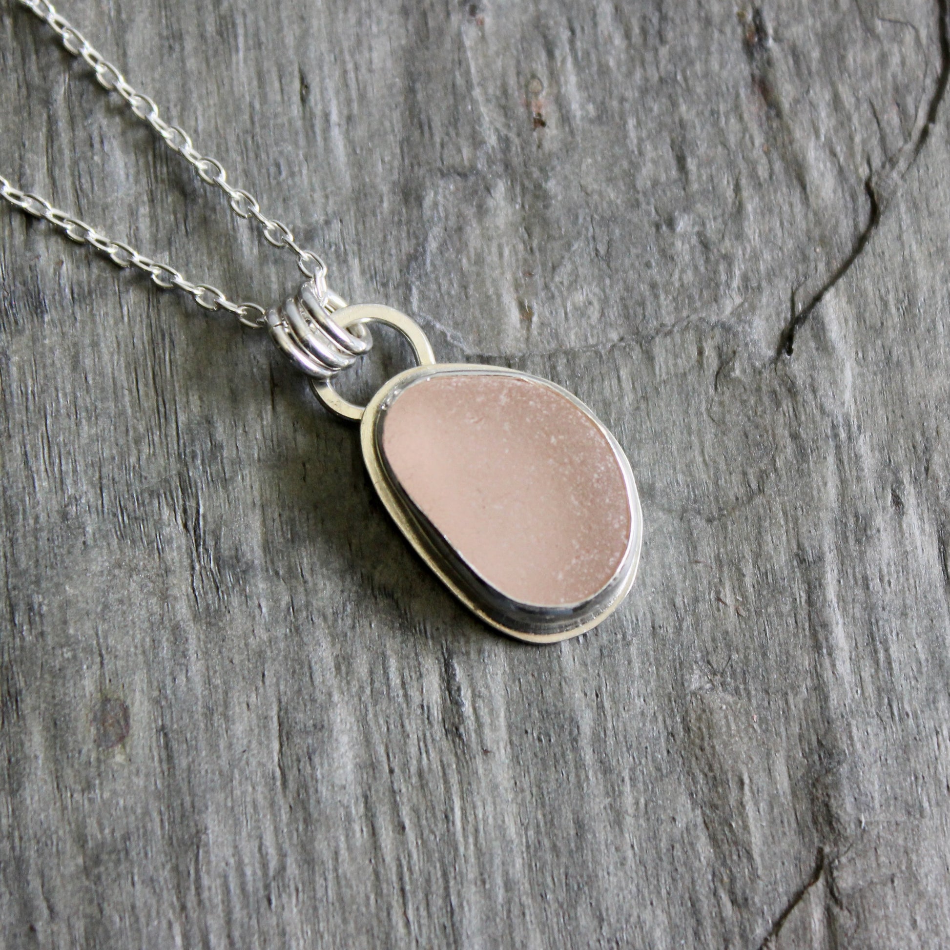 Necklace with a pink sea glass on a gray stone surface