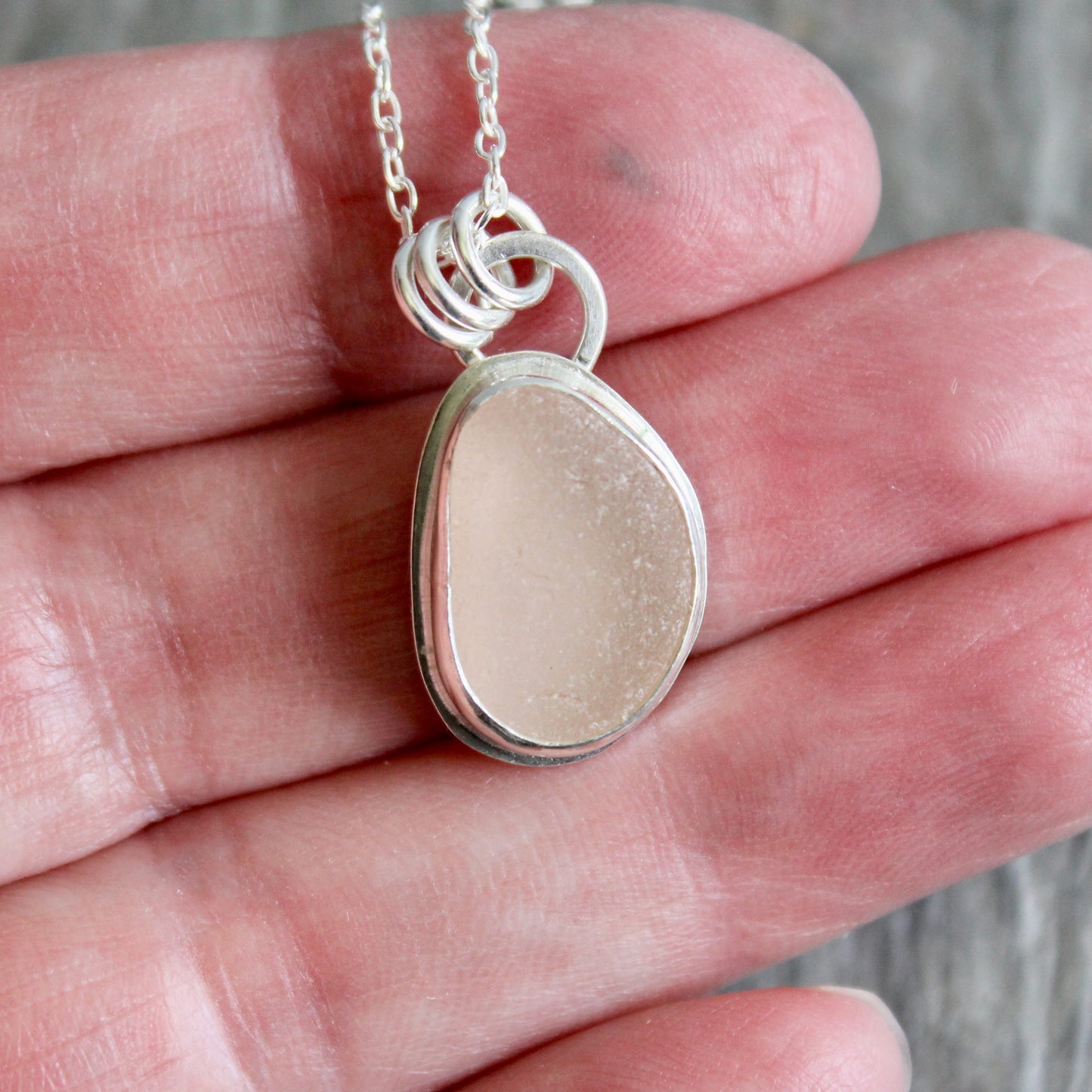 Silver necklace with a pink sea glass on a hand