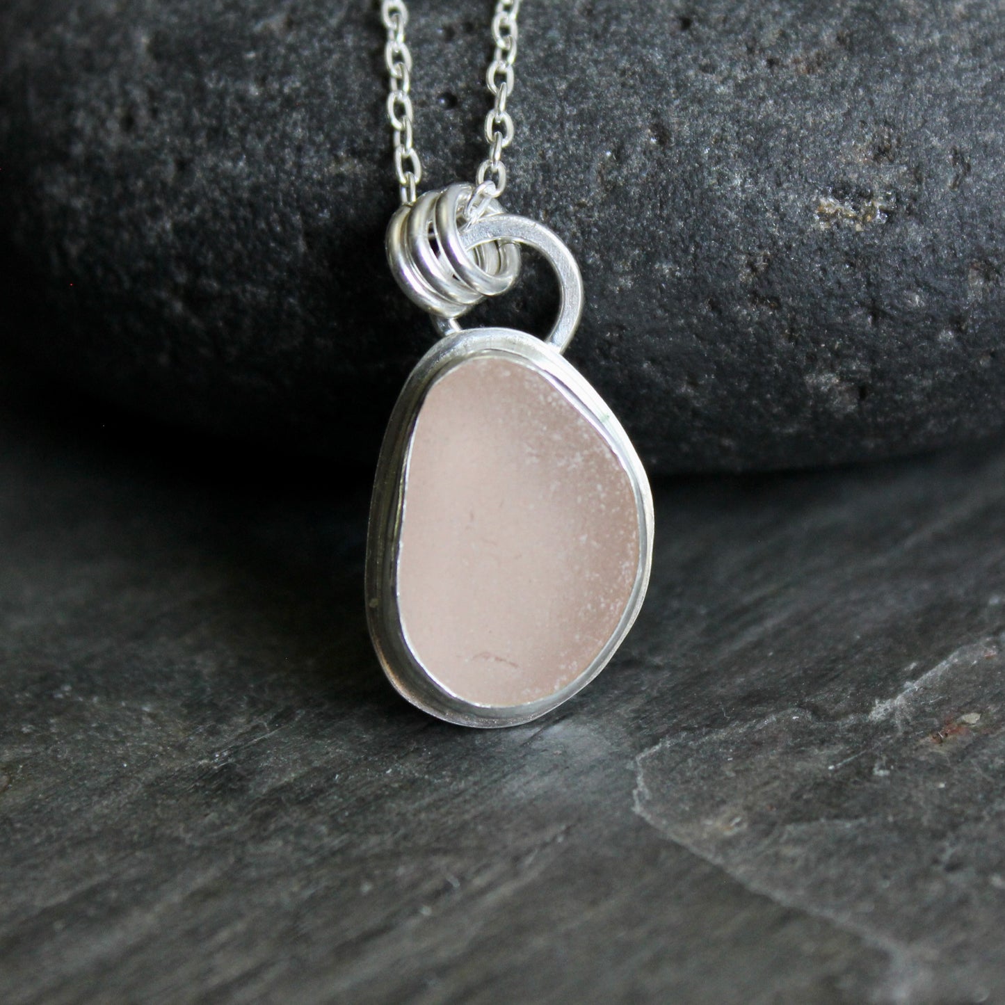 Silver necklace with a pink sea glass on a dark stone background