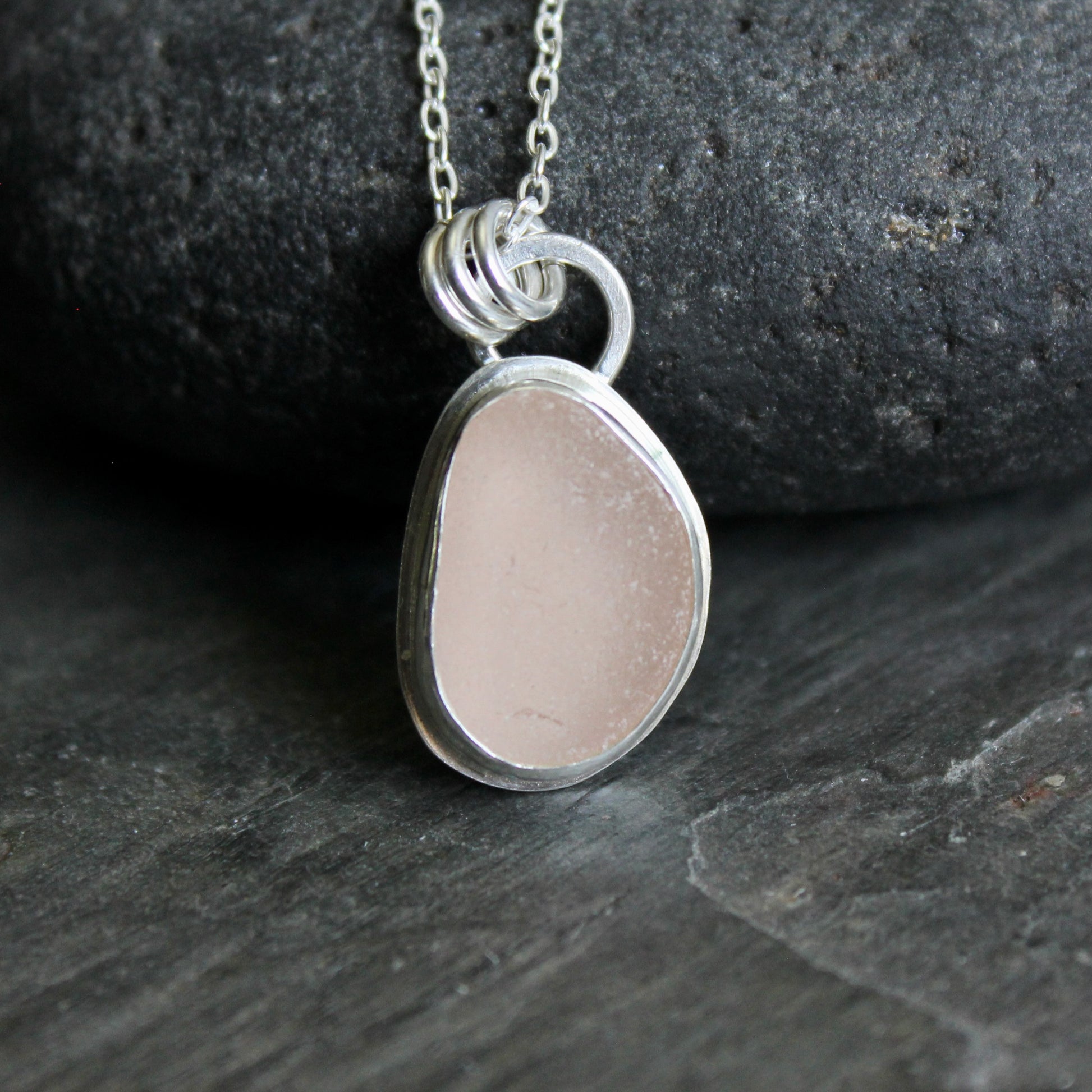 Silver necklace with a pink sea glass on a dark stone background