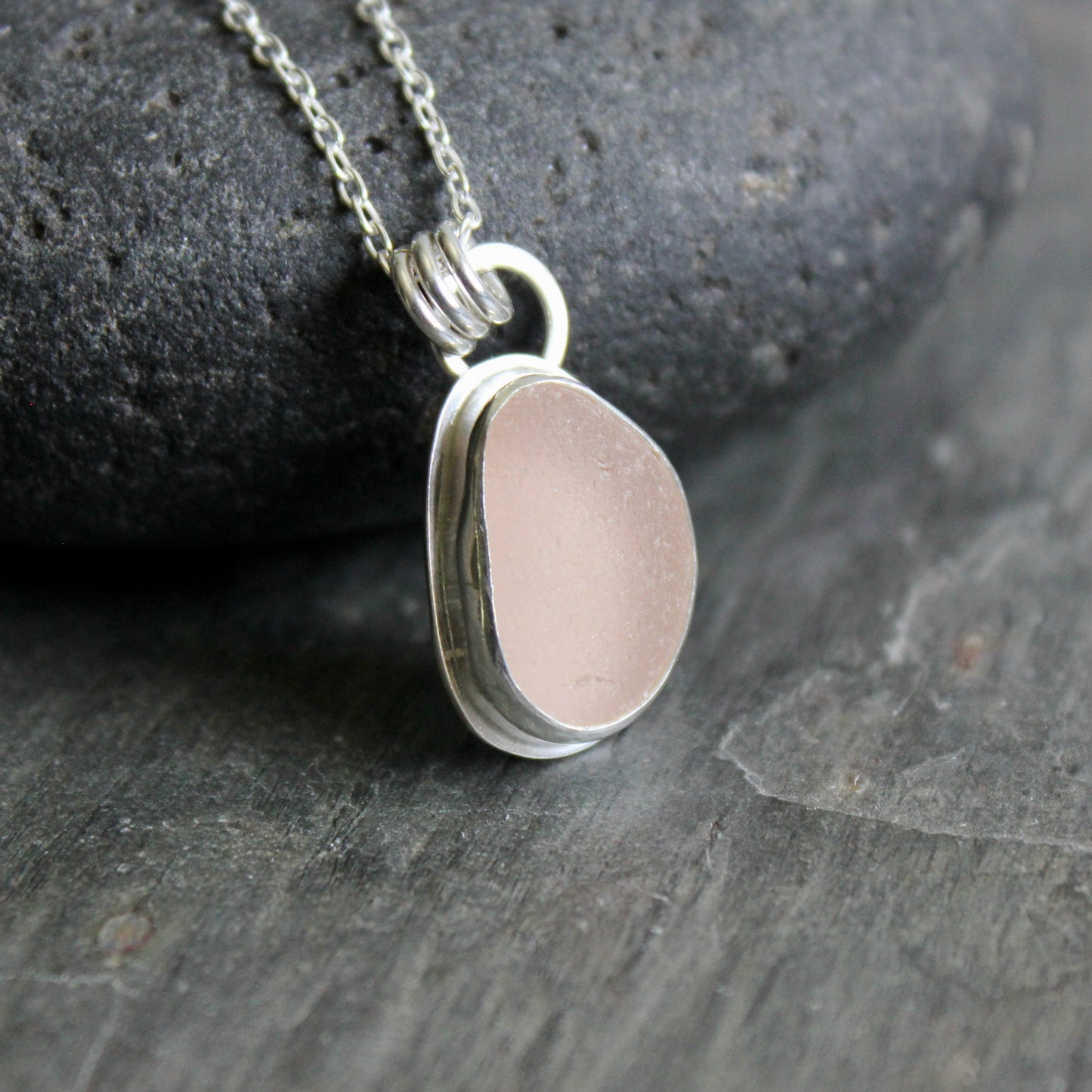 Pink sea glass necklace on a dark stone surface