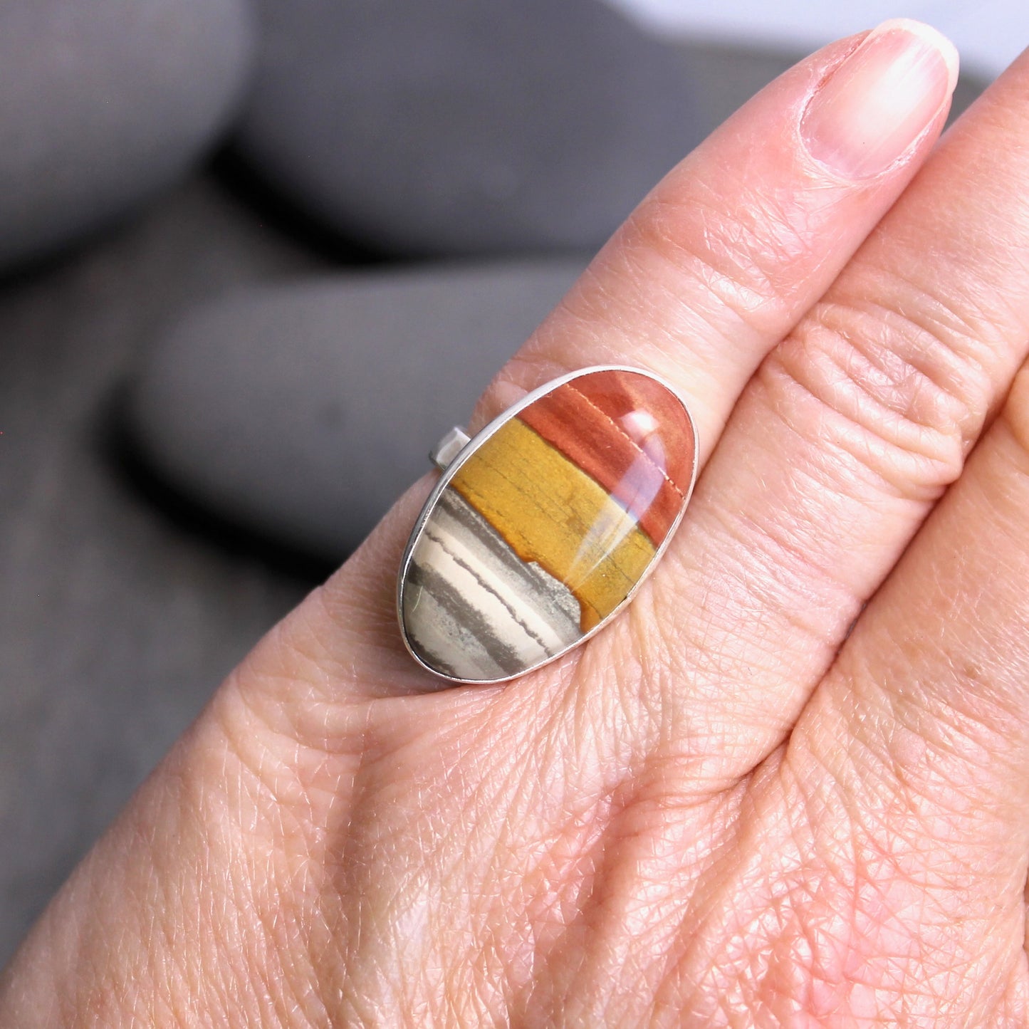 Hand wearing a ring with a multicolored stone on a blurred background