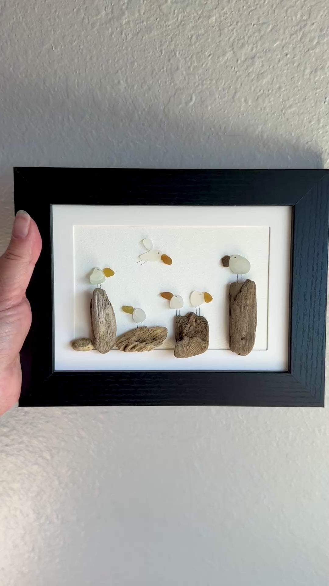Framed sea glass artwork made of sea glass and driftwood on a white surface.