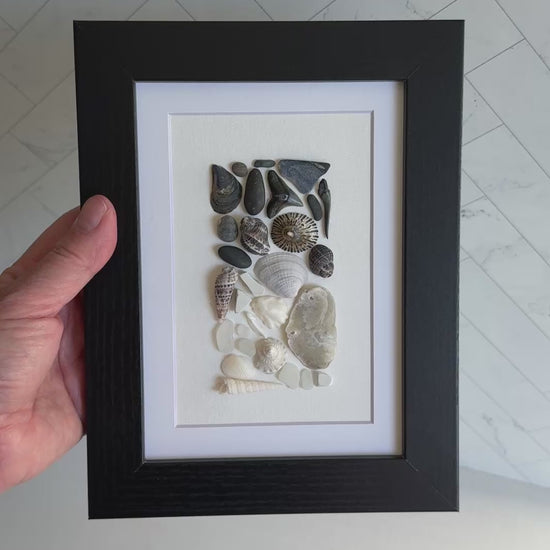 Framed artwork of pebbles, shells and sea glass on a white background