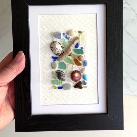 Framed artwork with seashells and sea glass pieces on a white background