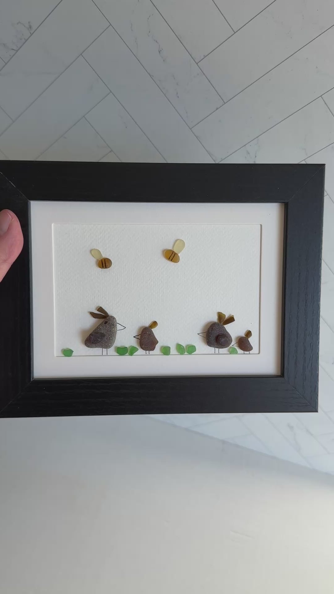 Framed sea glass artwork of hens and chickens on a white background with a black frame.