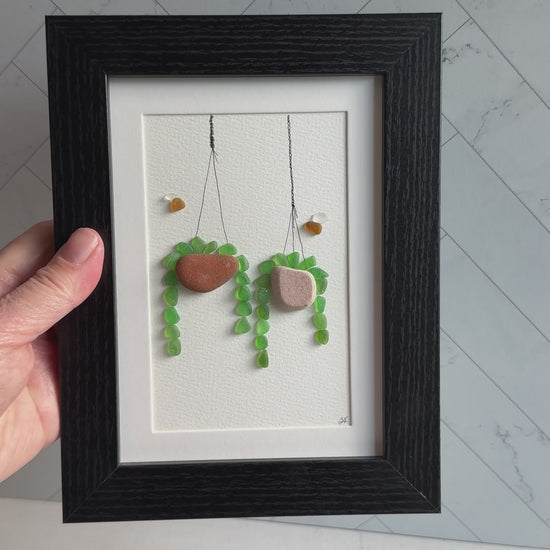 Framed sea glass artwork of hanging plants on a white background