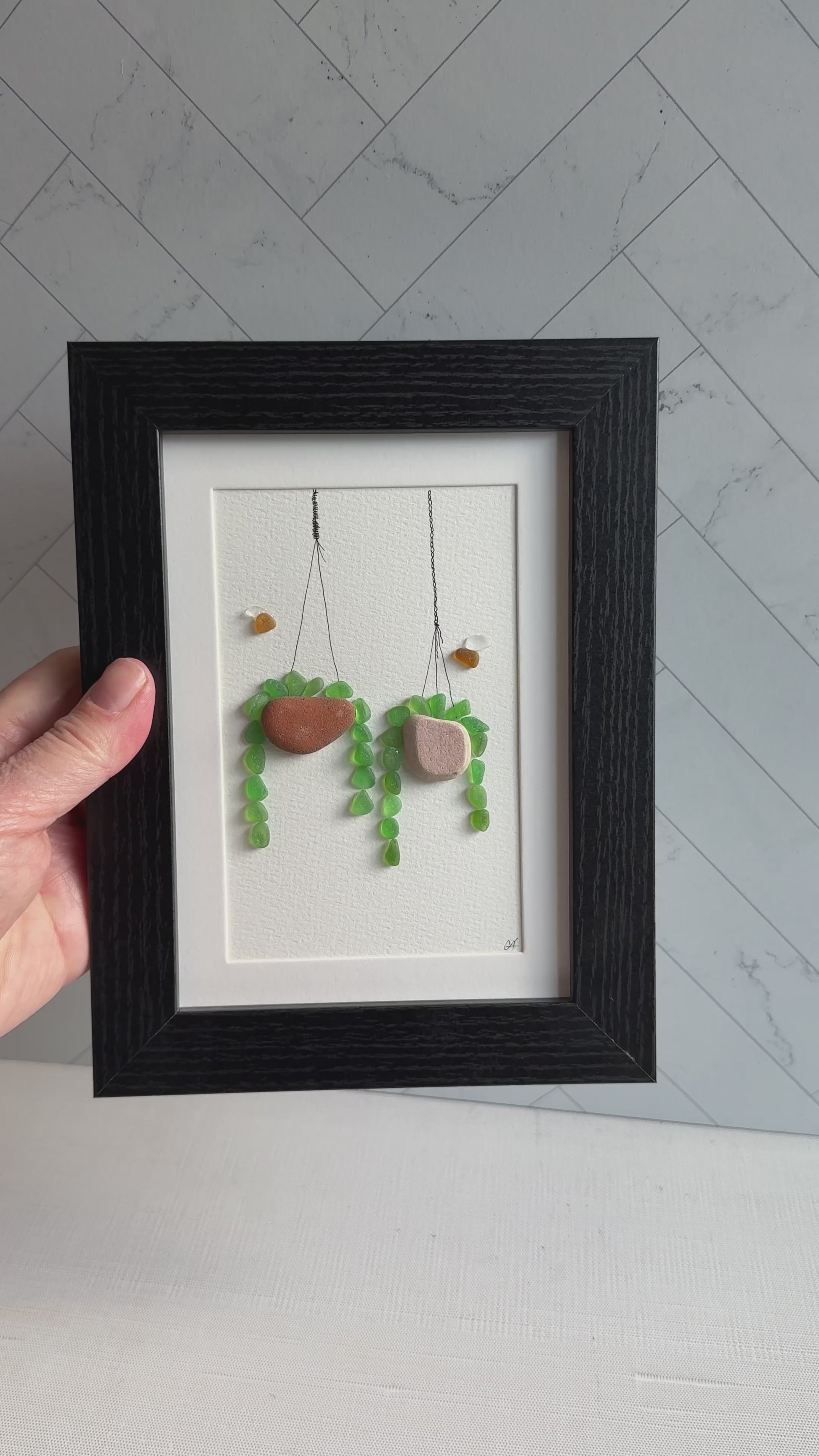 Framed sea glass artwork of hanging plants on a white background
