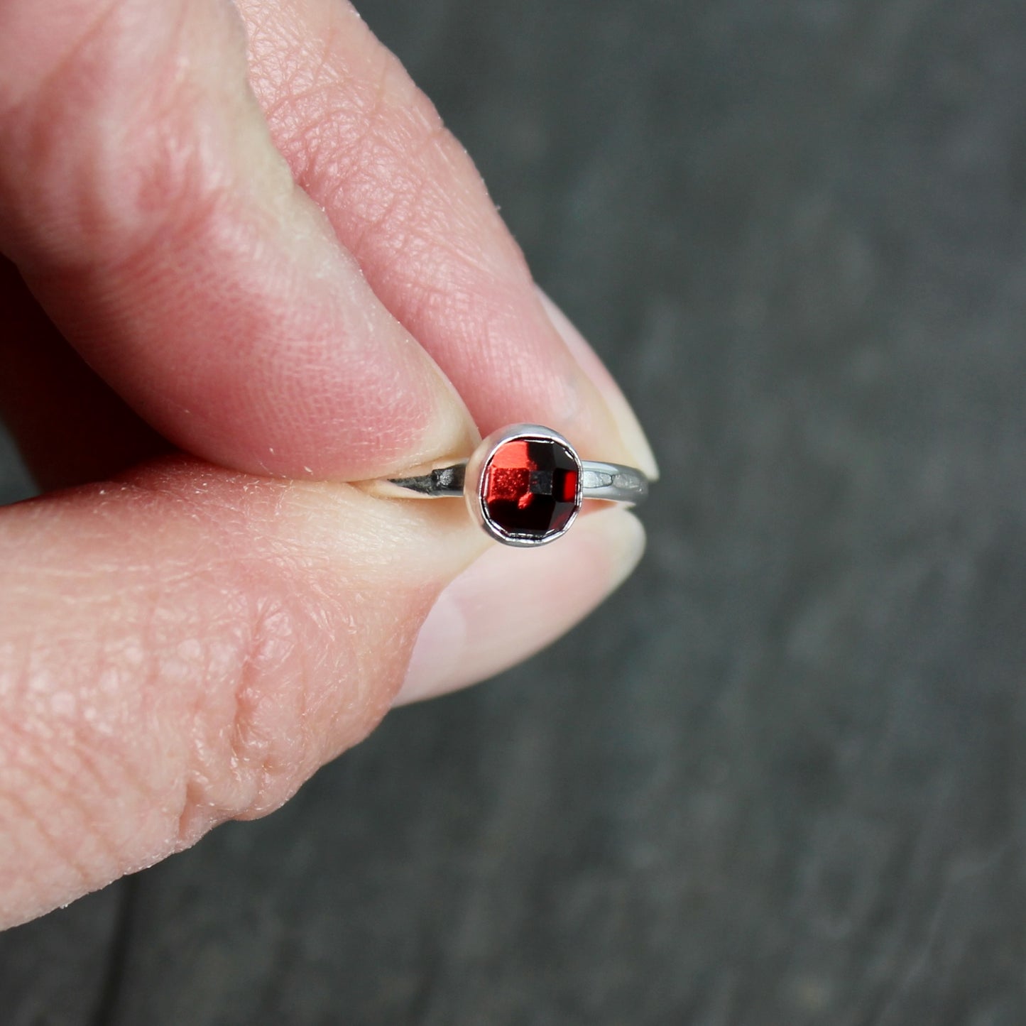 Silver ring with a red gemstone held between fingers against a dark background
