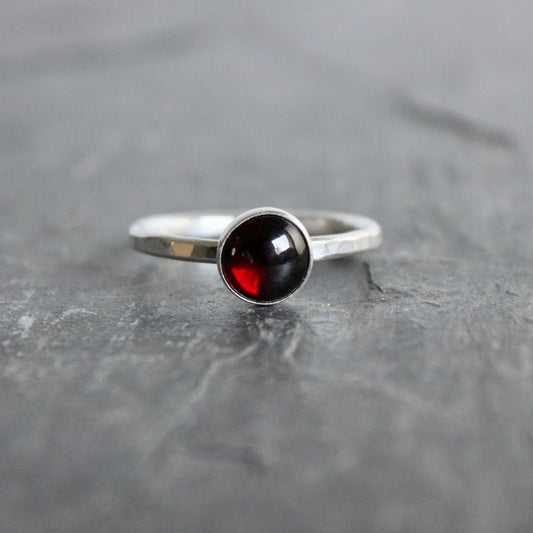 Silver ring with a black and red gemstone on a gray surface