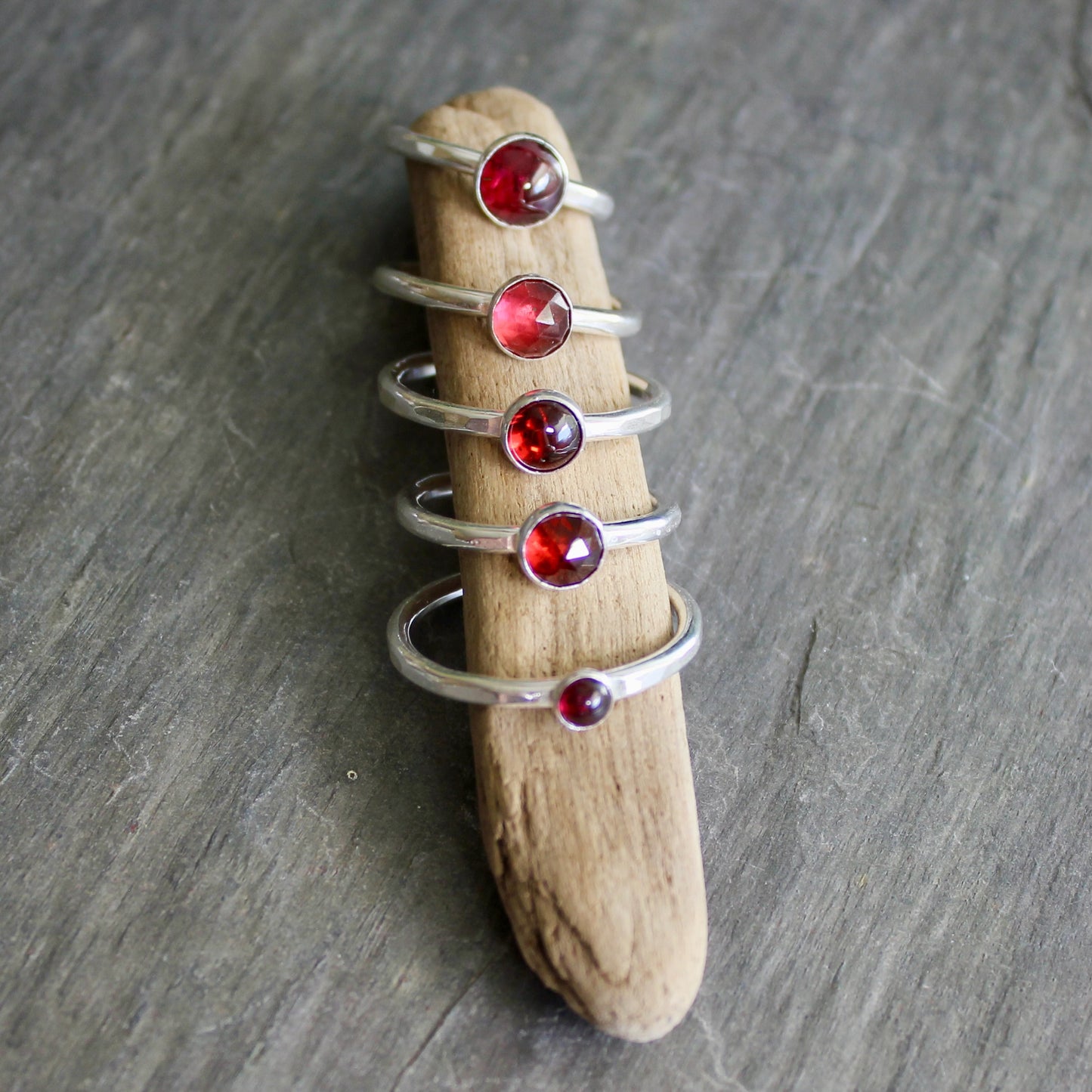Silver rings with red gemstones on a piece of driftwood against a gray background