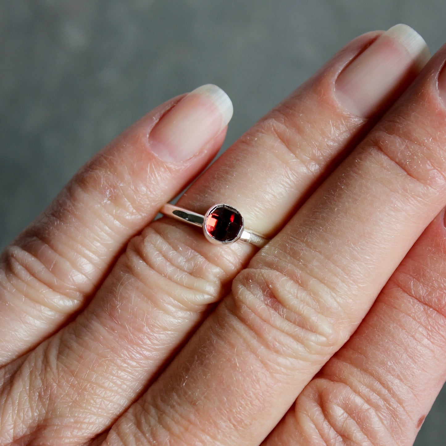 Silver ring with a red gemstone on a person's finger against a neutral background