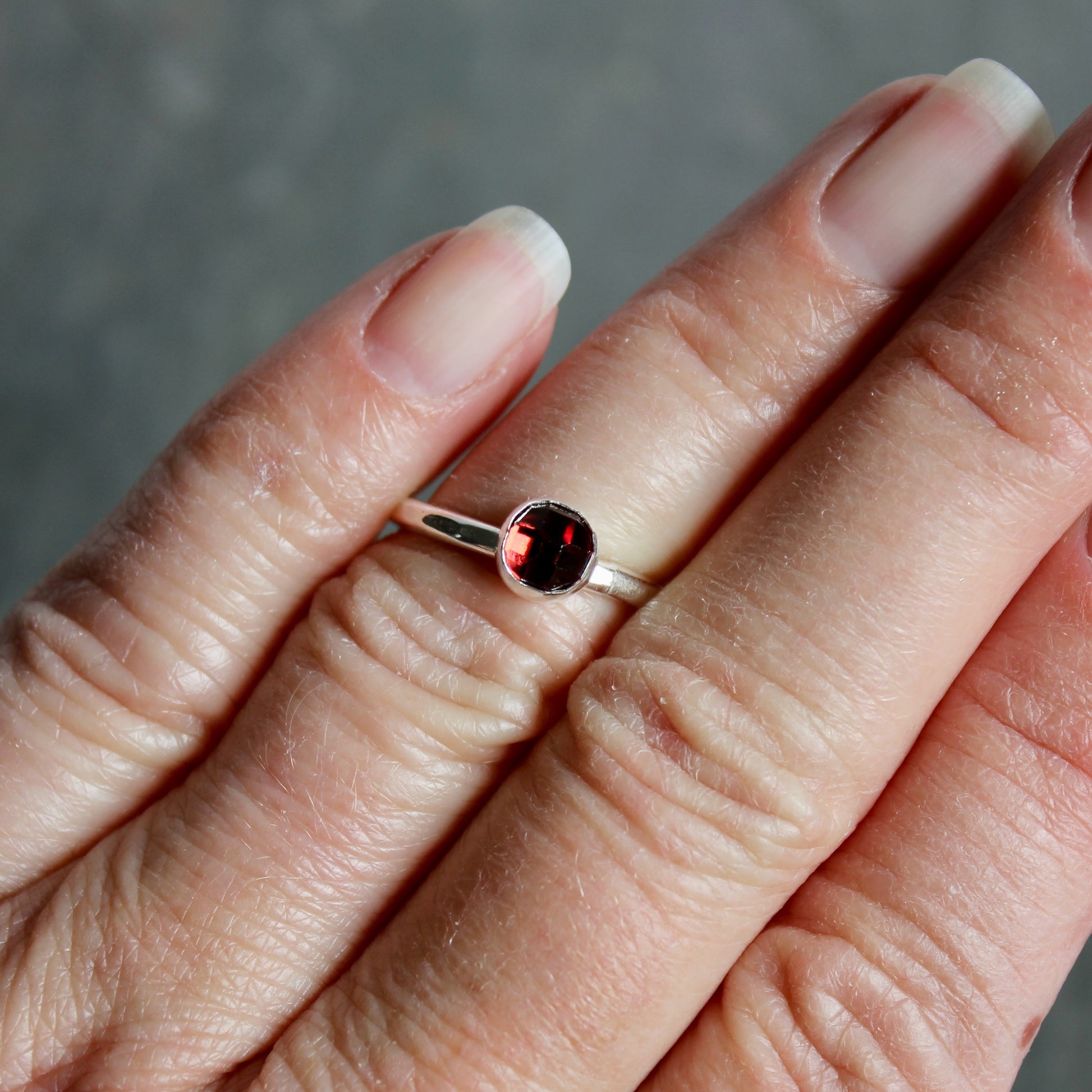 Silver ring with a red gemstone on a person's finger against a neutral background