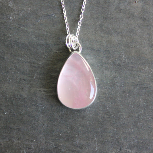 Pink teardrop pendant on a silver chain against a dark gray background
