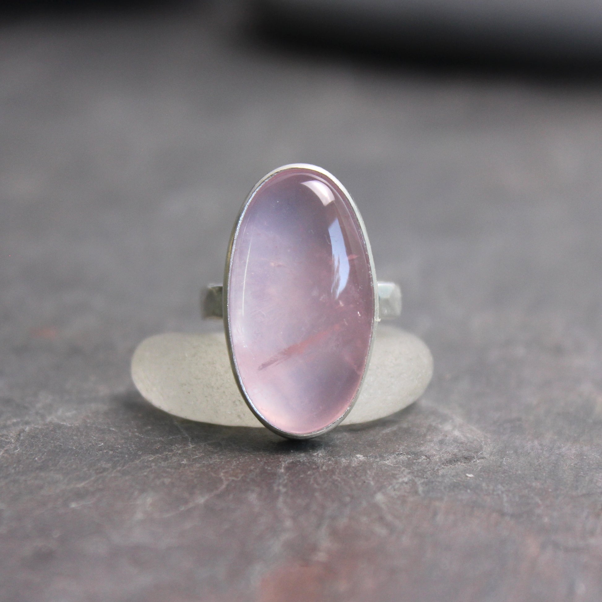 Ring with a rose quartz oval stone on a dark gray surface