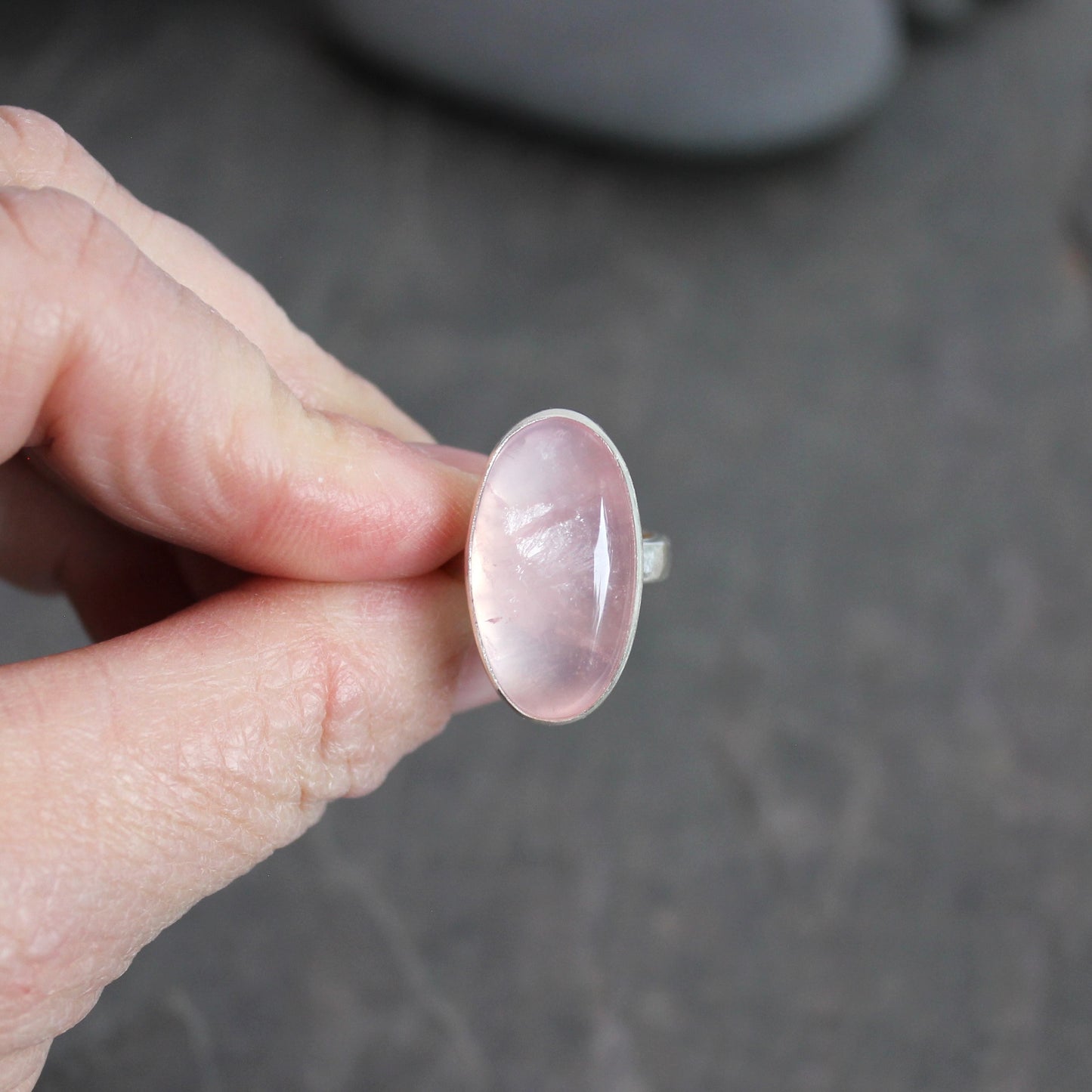 Hand holding a rose quartz ring against a dark background
