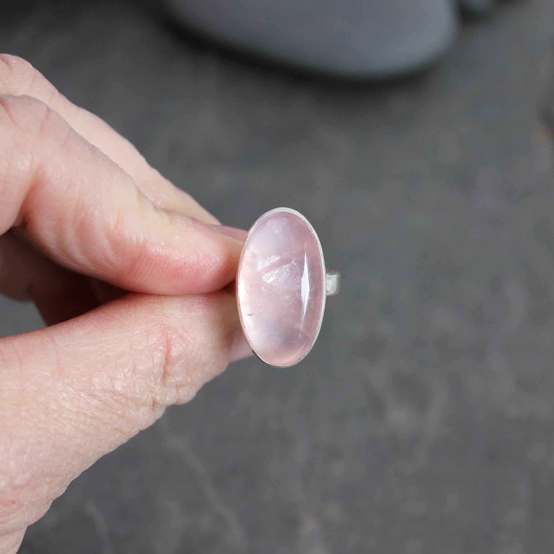 Hand holding a rose quartz ring against a dark background