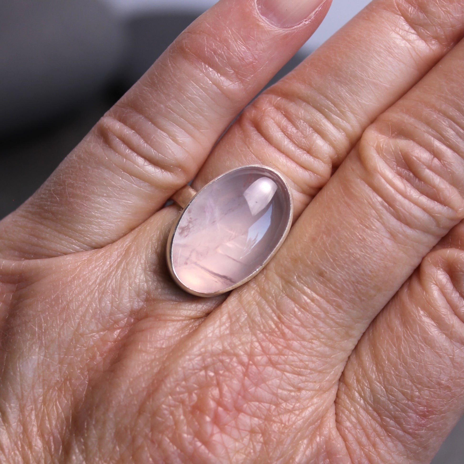Close-up of a hand wearing a ring with a pink rose quartz stone