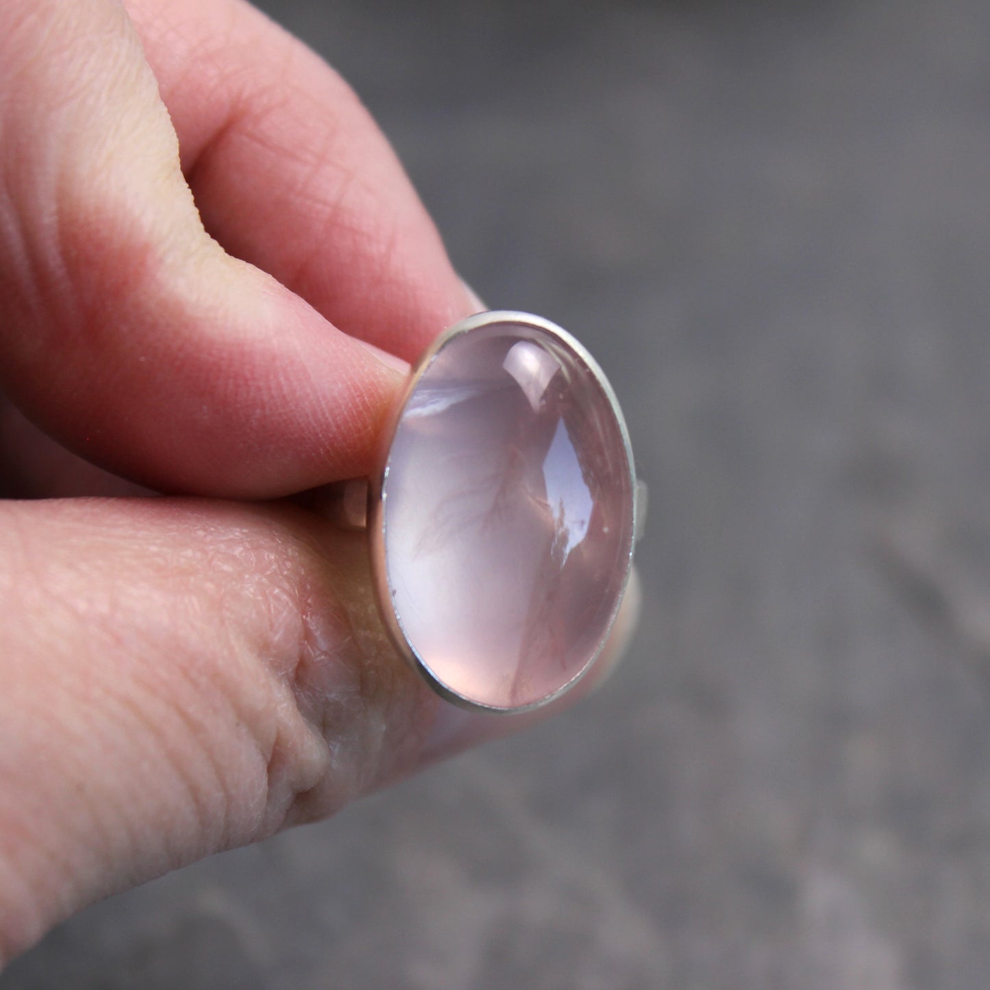 Hand holding a silver ring with a pink rose quartz stone against a blurred background